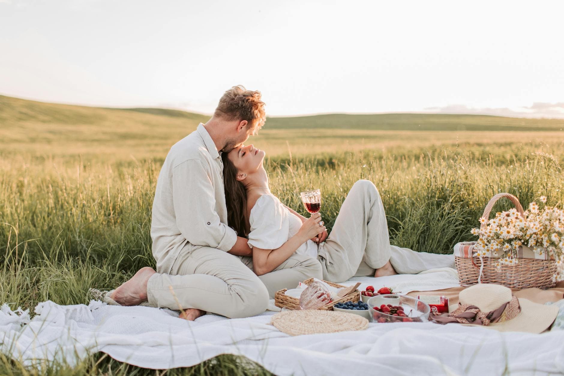 A couple enjoying a romantic picnic in a serene grassy field at sunset, surrounded by nature. - spring dating refresh