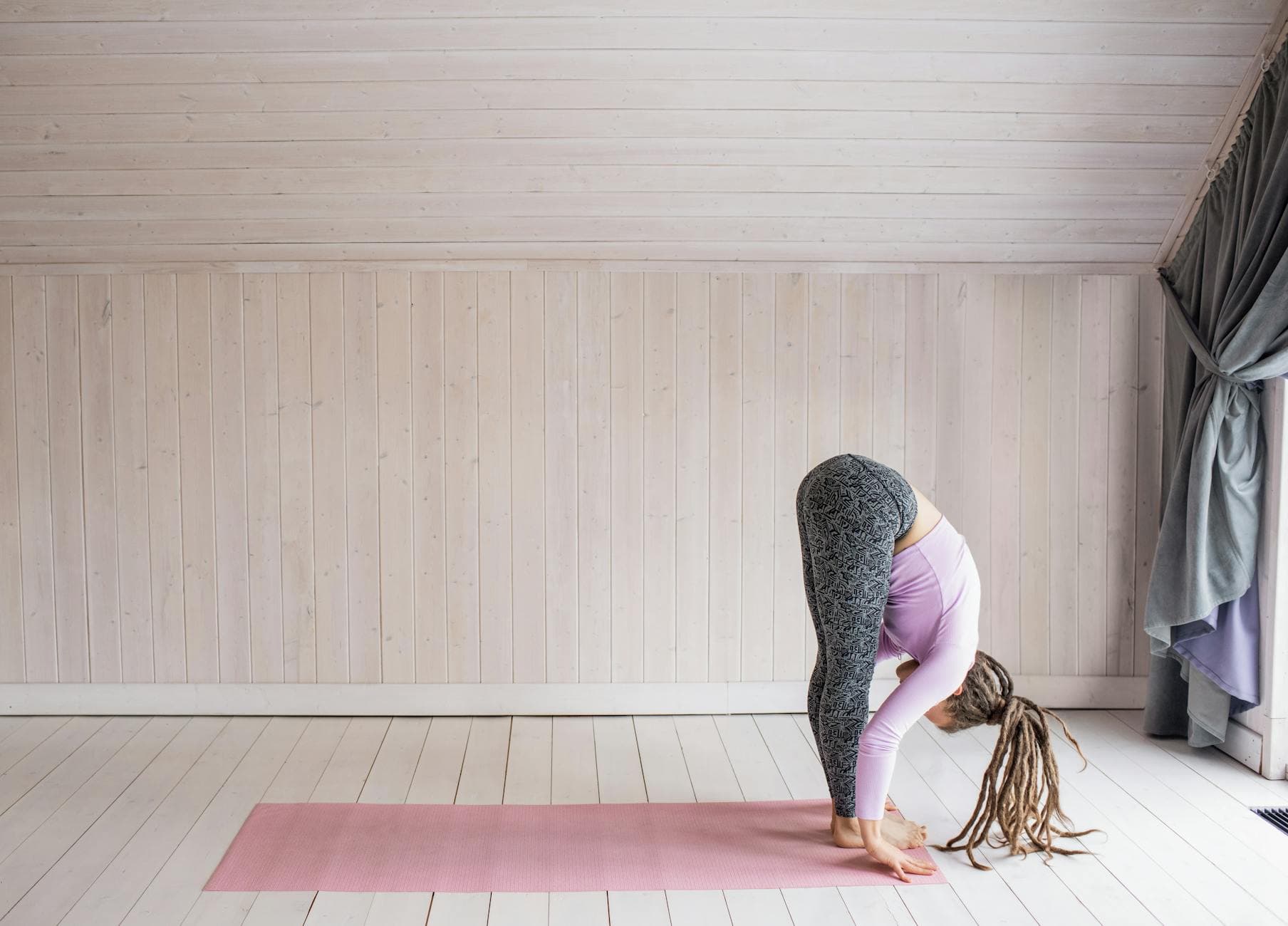 A woman doing a forward bend yoga pose on a pink mat in a serene indoor setting. - spring forward mental health