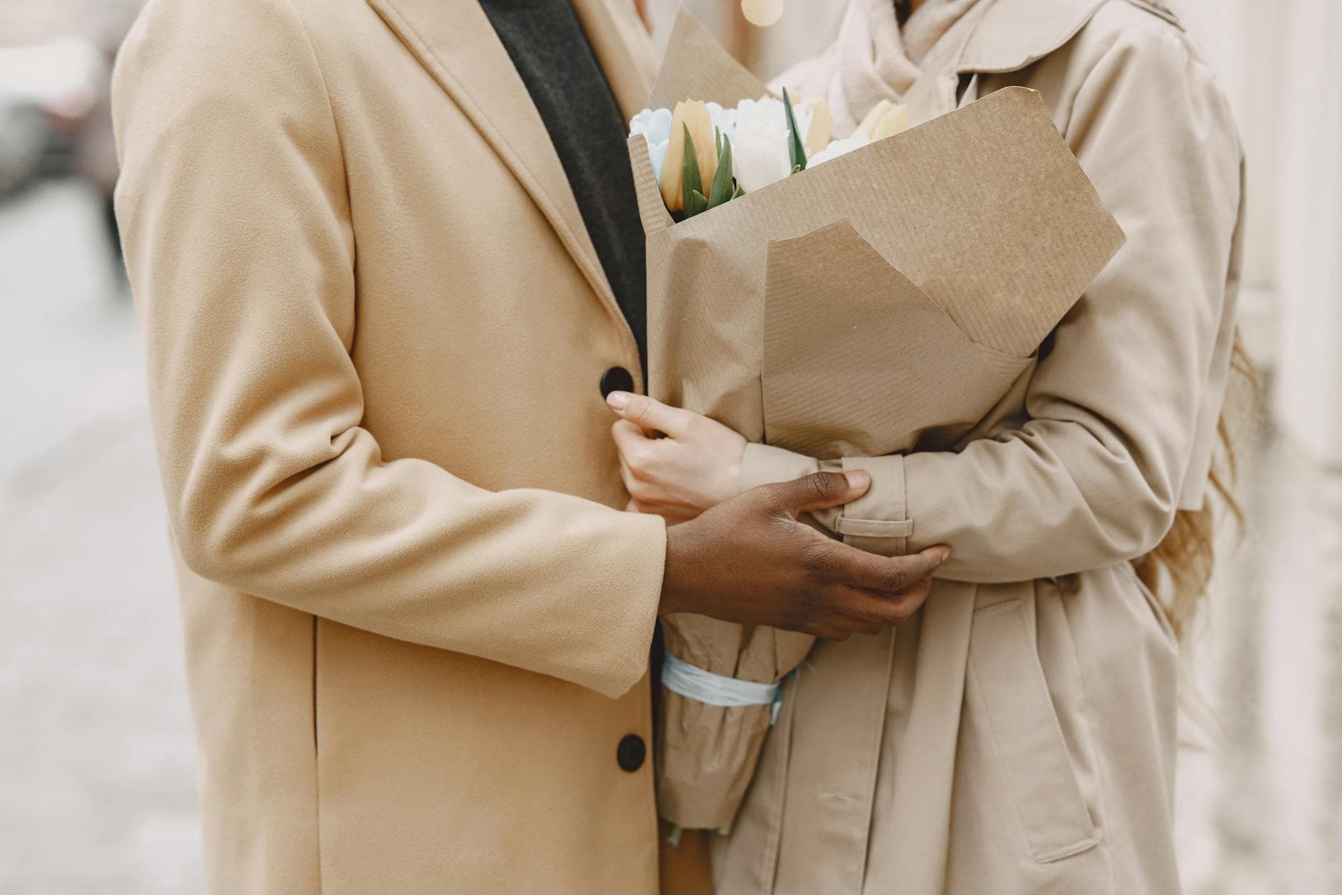 Close-up of a couple in coats holding a tulip bouquet, embracing outdoors. - spring relationship reconnection