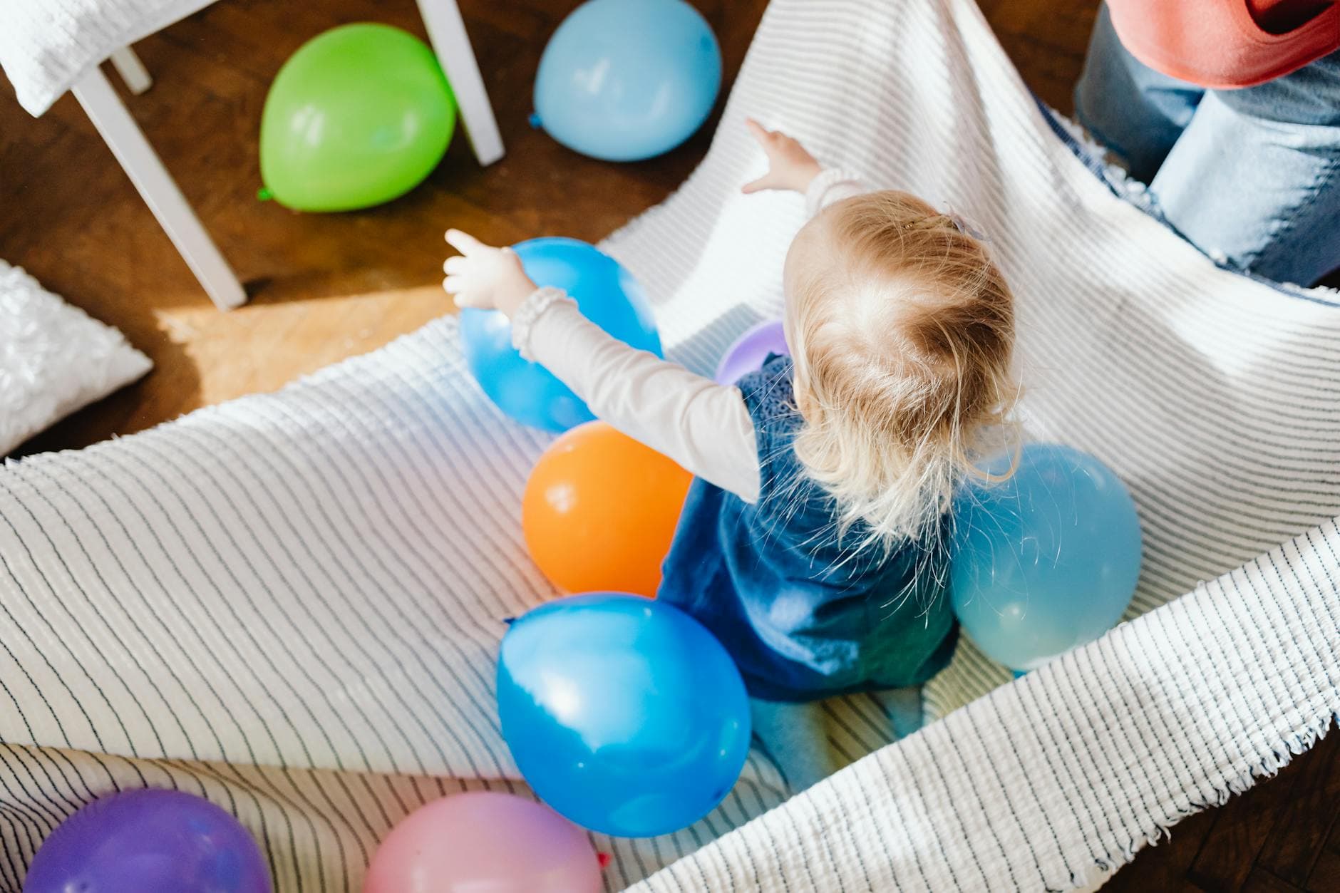 A toddler enjoying playtime with vibrant balloons indoors, creating a joyful scene. - toddler independence activities