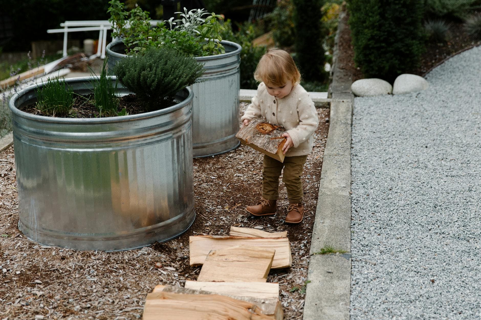 Young child exploring outdoors with logs and garden planters in a natural setting. - toddler outdoor independence