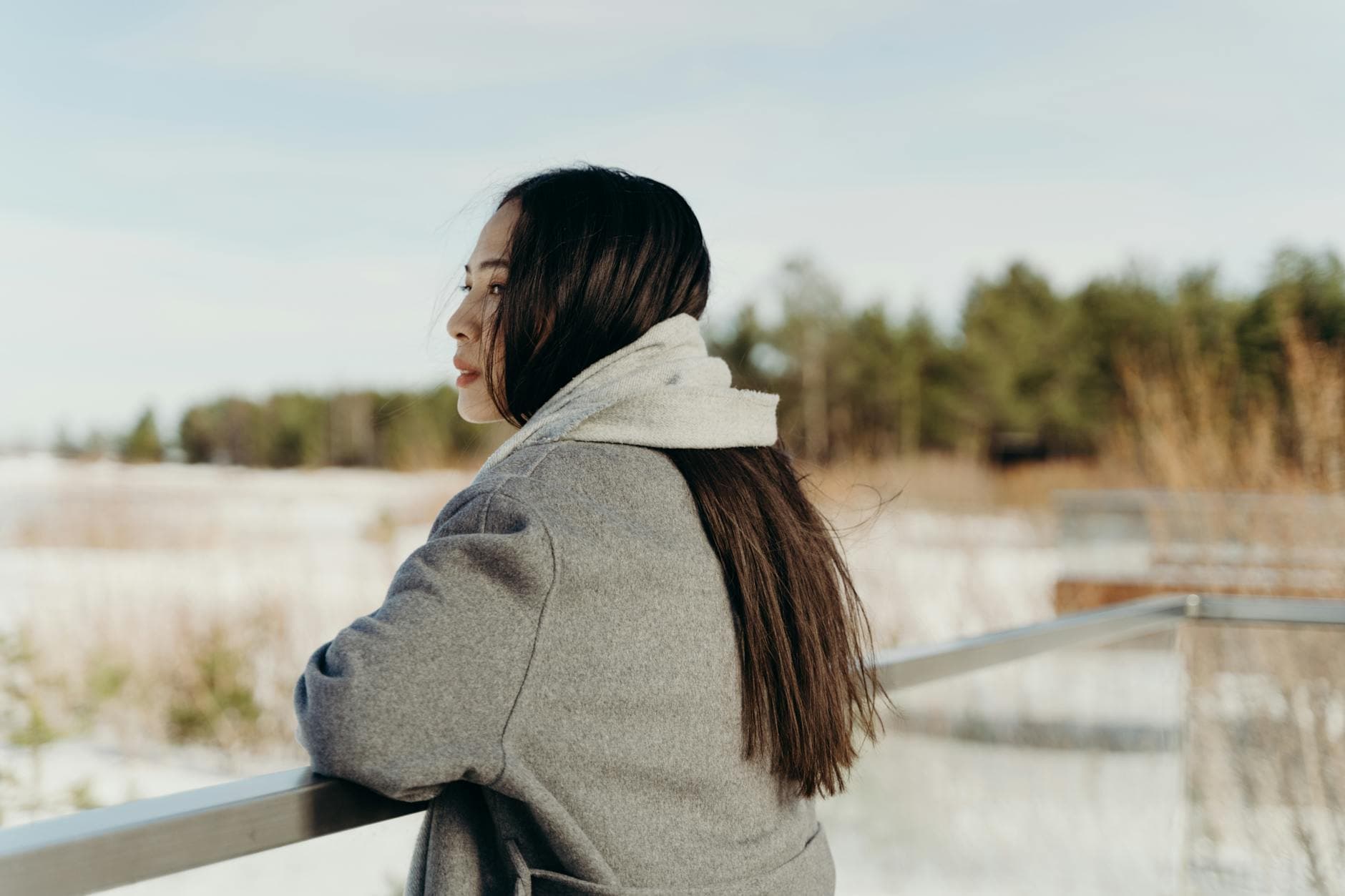 A woman in a warm coat looks out over a snowy landscape, enjoying the serene winter atmosphere. - winter sadness therapy
