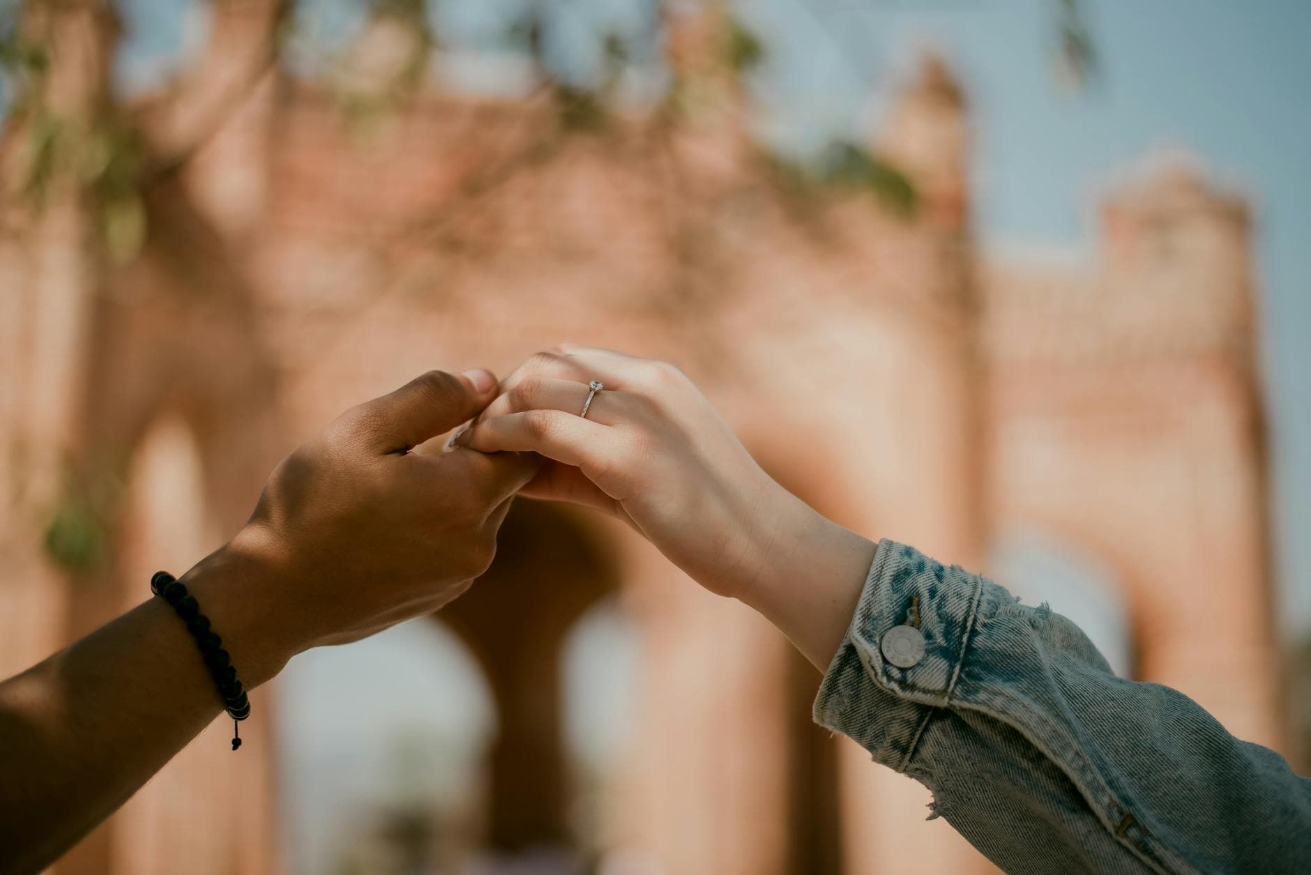 Close-up of a couple's hands with focus on a ring, set against a historic arch background outdoors. - casual to committed relationship