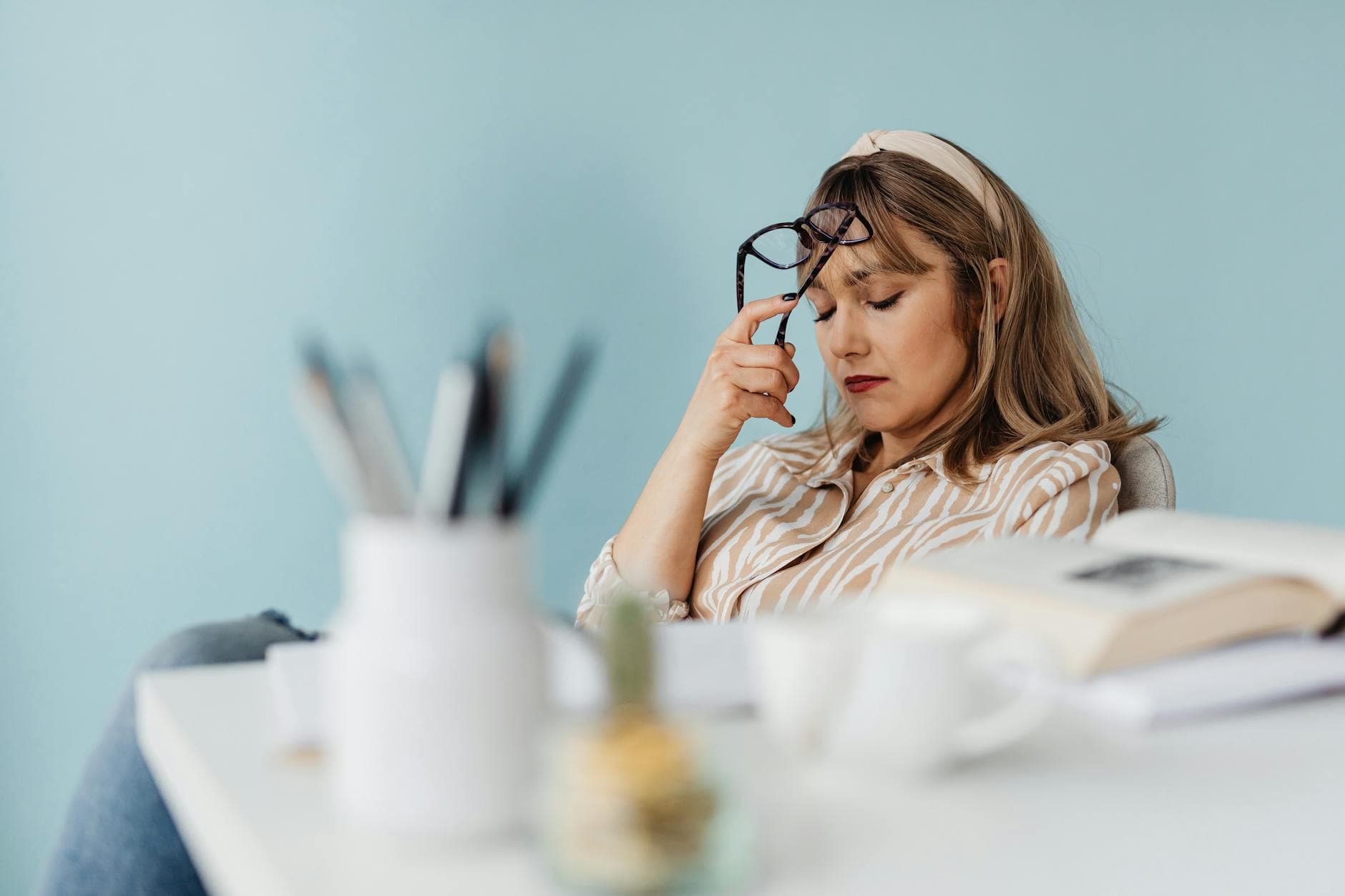 Caucasian woman looks exhausted while taking a break with eyes closed at her desk. - mental health decluttering
