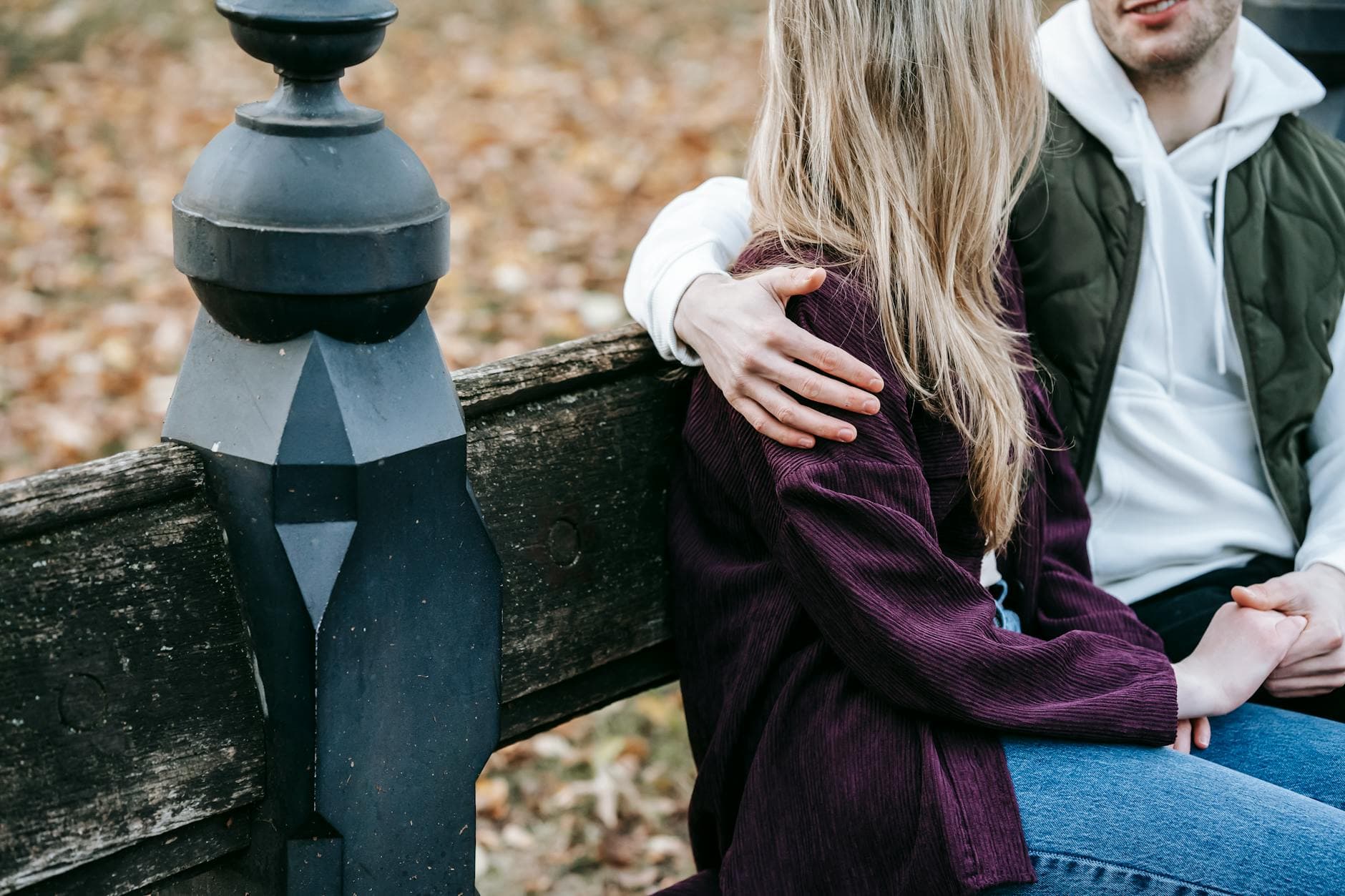 Crop anonymous loving couple resting on bench while holding hands in park with autumn leaves - repairing trust after fight