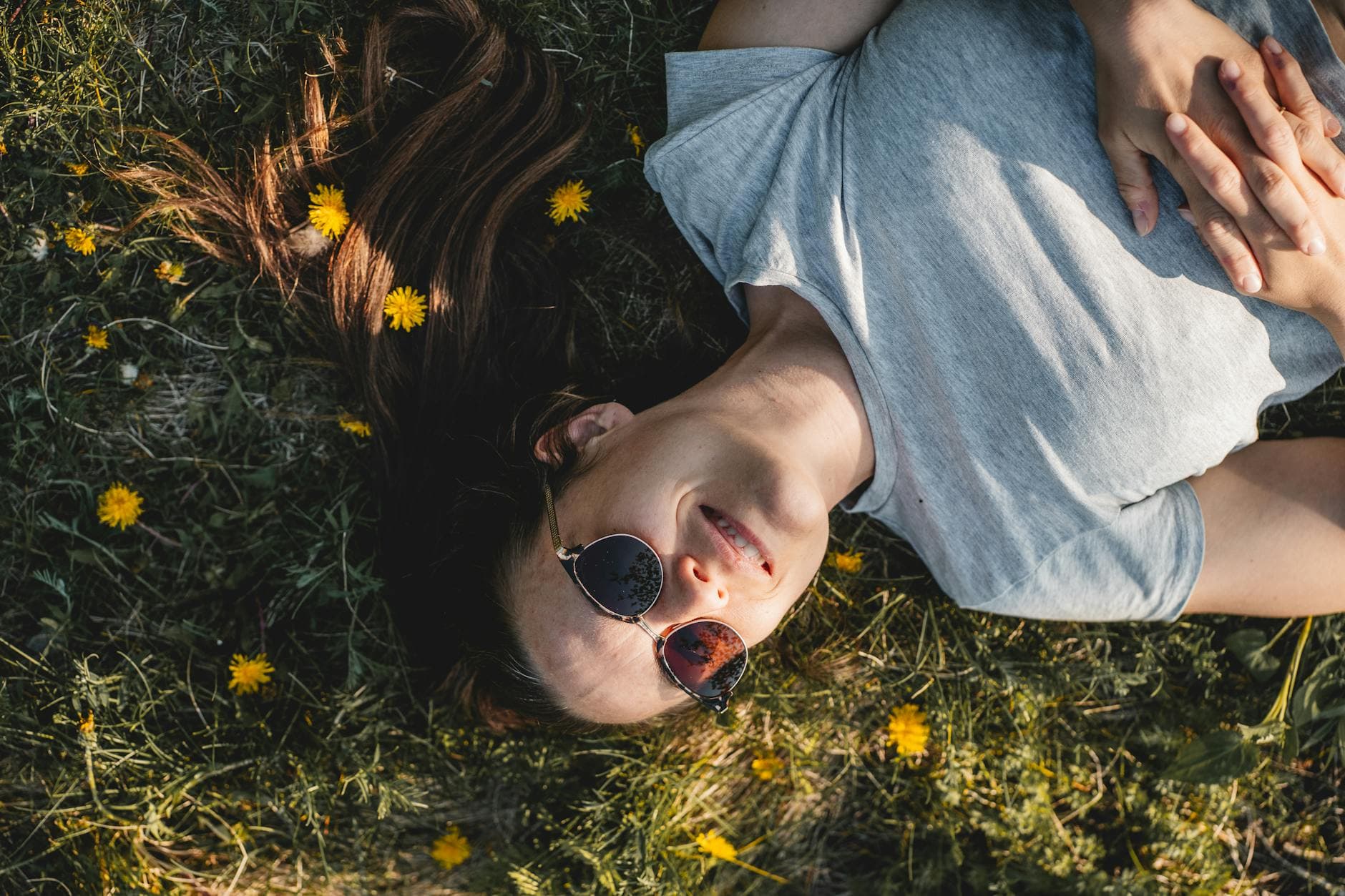 A woman enjoying a sunny day lying in a meadow full of dandelions in Québec, Canada wearing sunglasses. - spring burnout recovery