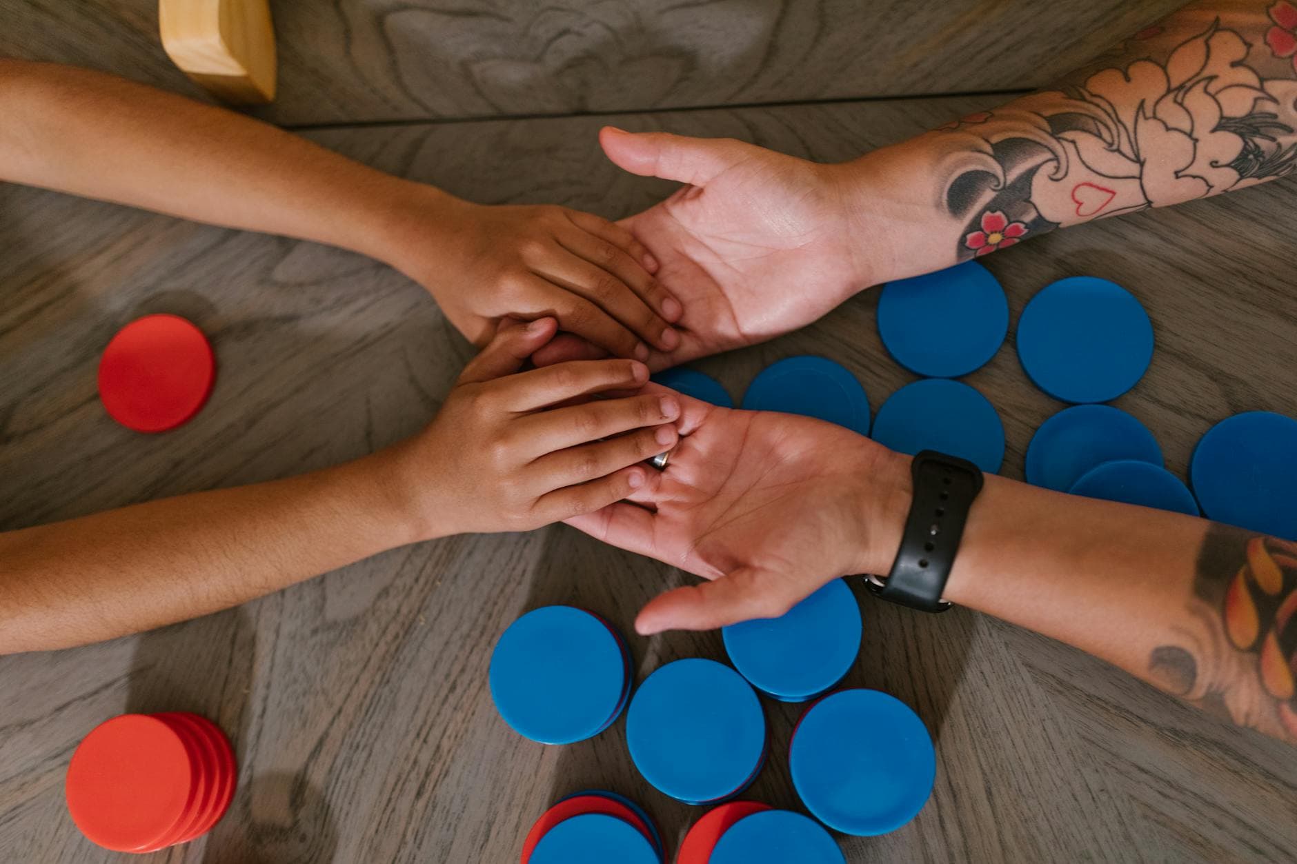 Close-up of hands holding while playing a game with blue and red chips on a table. - therapy integration skills