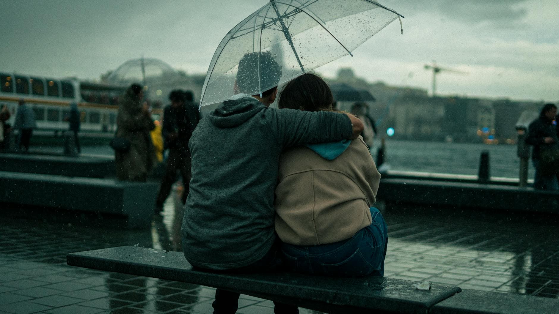 A couple sits close under an umbrella, embracing on a rainy city day. - vulnerability in relationships