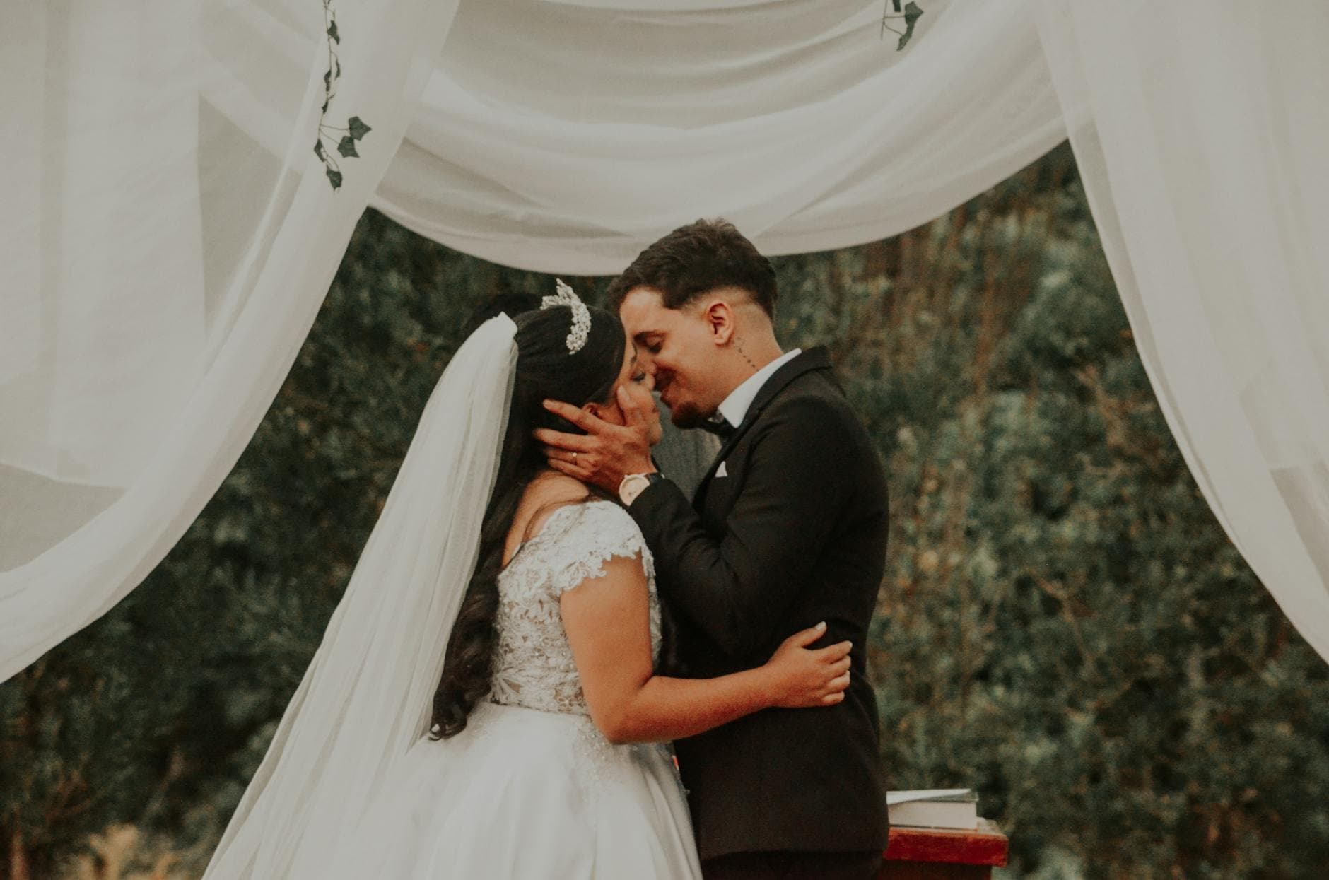 Bride and groom share a romantic kiss during an outdoor wedding ceremony surrounded by elegant drapery. - marriage growth strategies