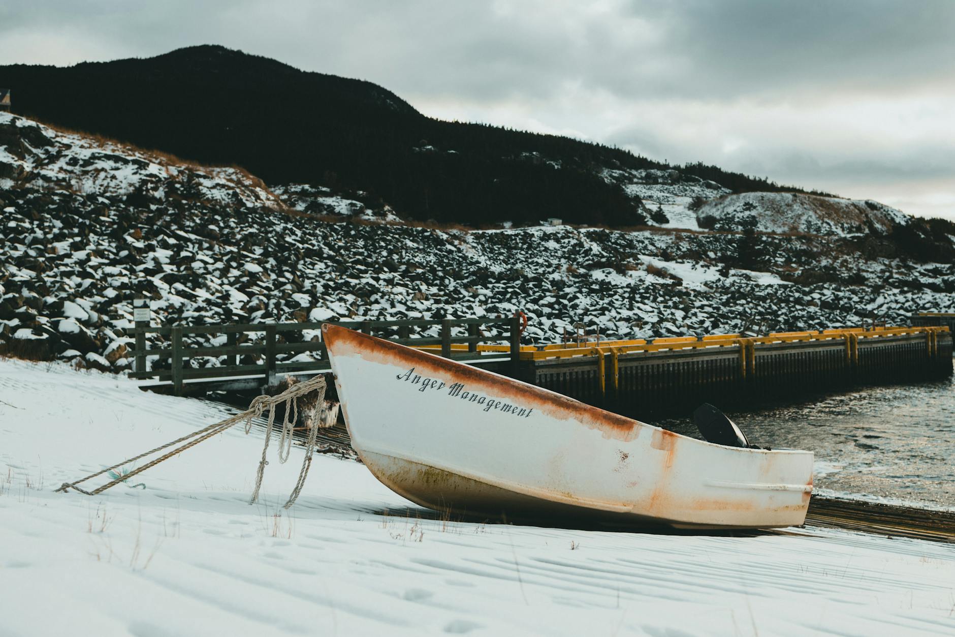 Rustic boat named 'Anger Management' resting on snowy shore by a rocky landscape. - anger management cast