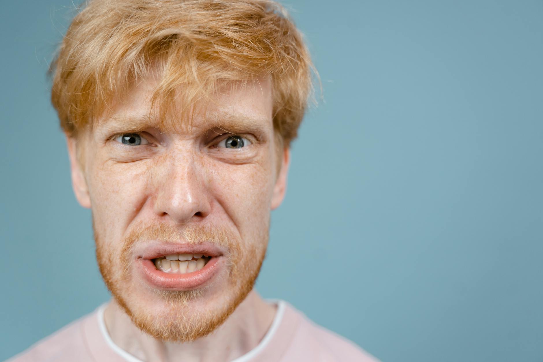 Close-up of a redhead man showing an intense facial expression against a blue background. - anger management techniques