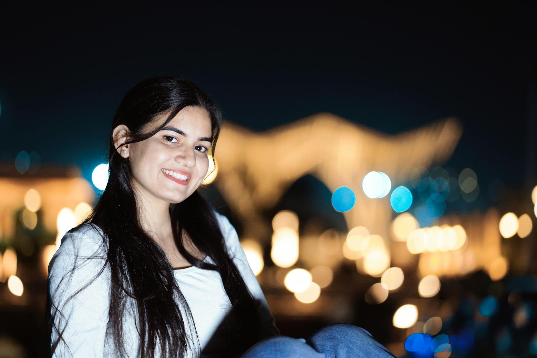 A young woman smiling against a blurry city lights backdrop at night. - how to apologize to boyfriend