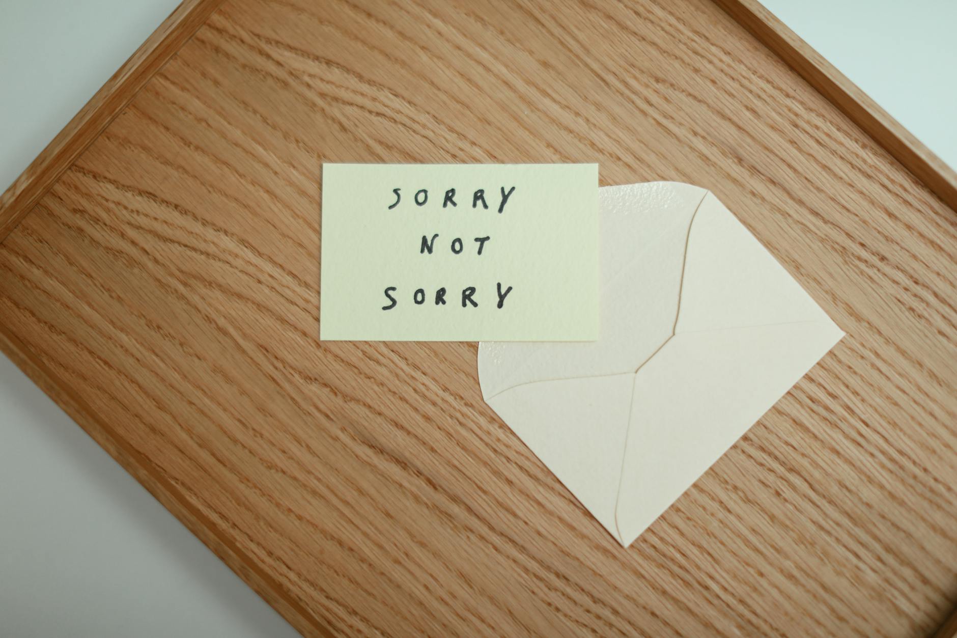 A flat lay of a 'Sorry Not Sorry' card with an envelope on a wooden surface. - apologize to a friend