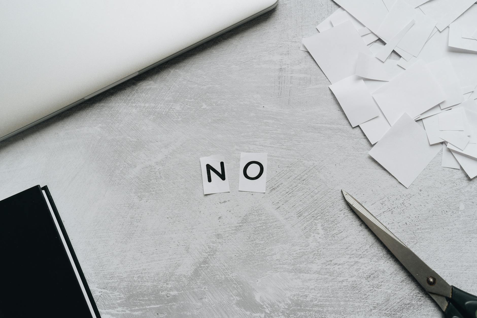Top view of scattered paper squares, laptop, and scissors forming the word 'NO', implying rejection or denial. - how to apologize professionally