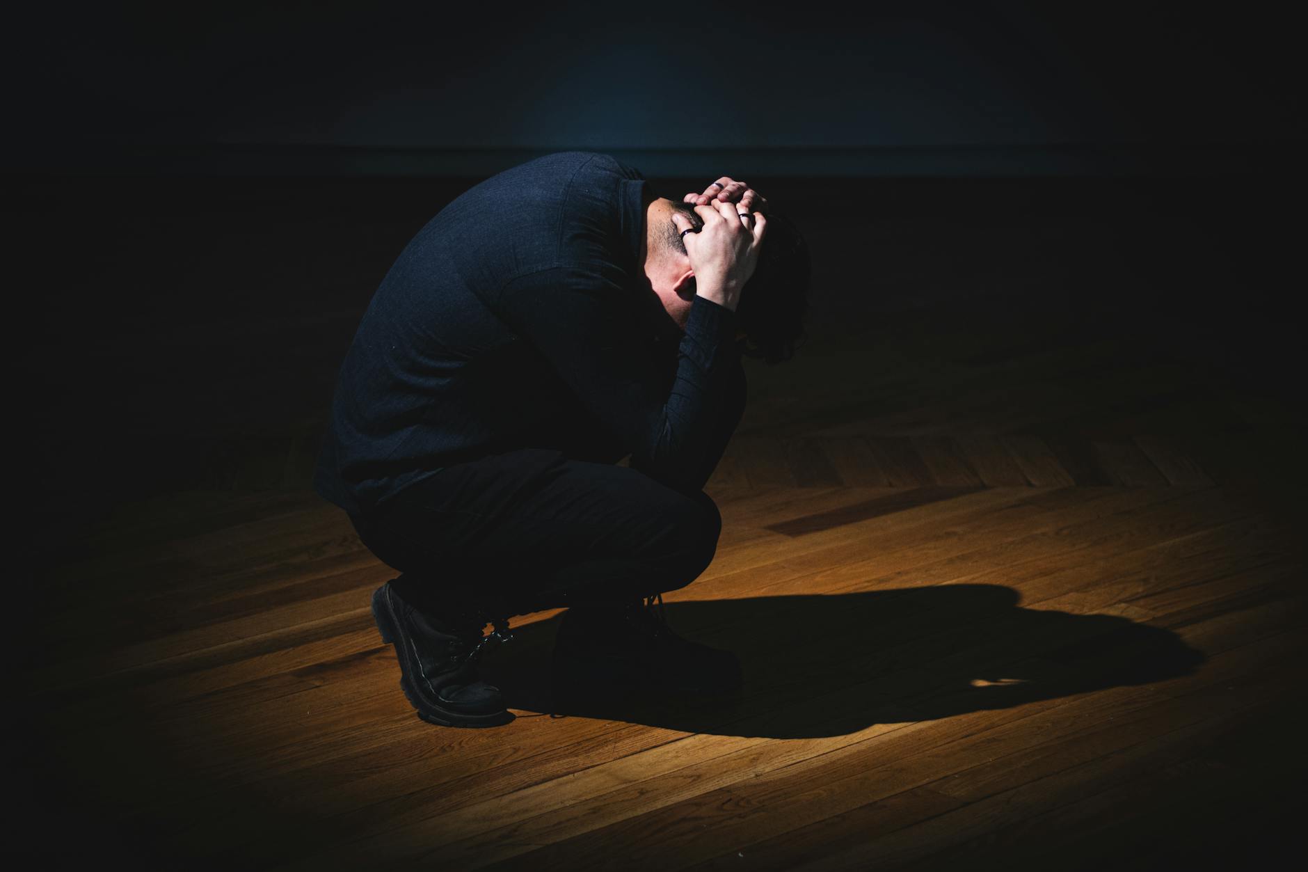 Person in dark room under spotlight, symbolizing solitude and introspection. - what causes anxiety disorder