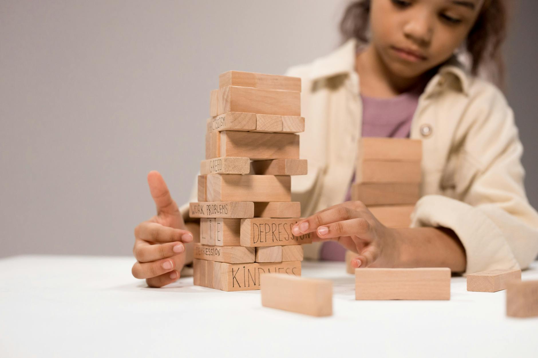 A child thoughtfully stacks wooden blocks with words like 'depression' and 'kindness.' - child social emotional development break