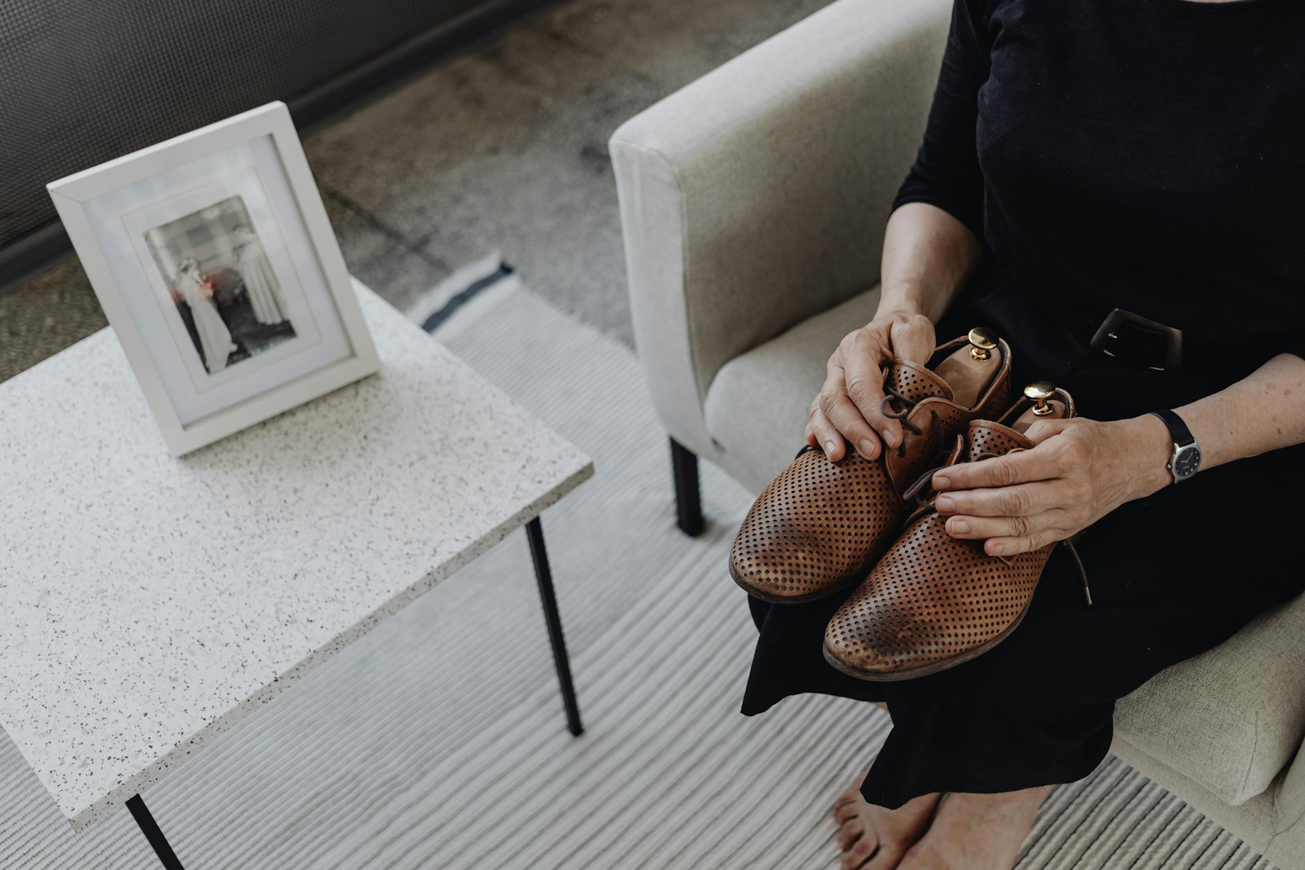 A person in black clothing holds shoes while seated, reflecting on loss beside a framed photo. - coping with grief in winter