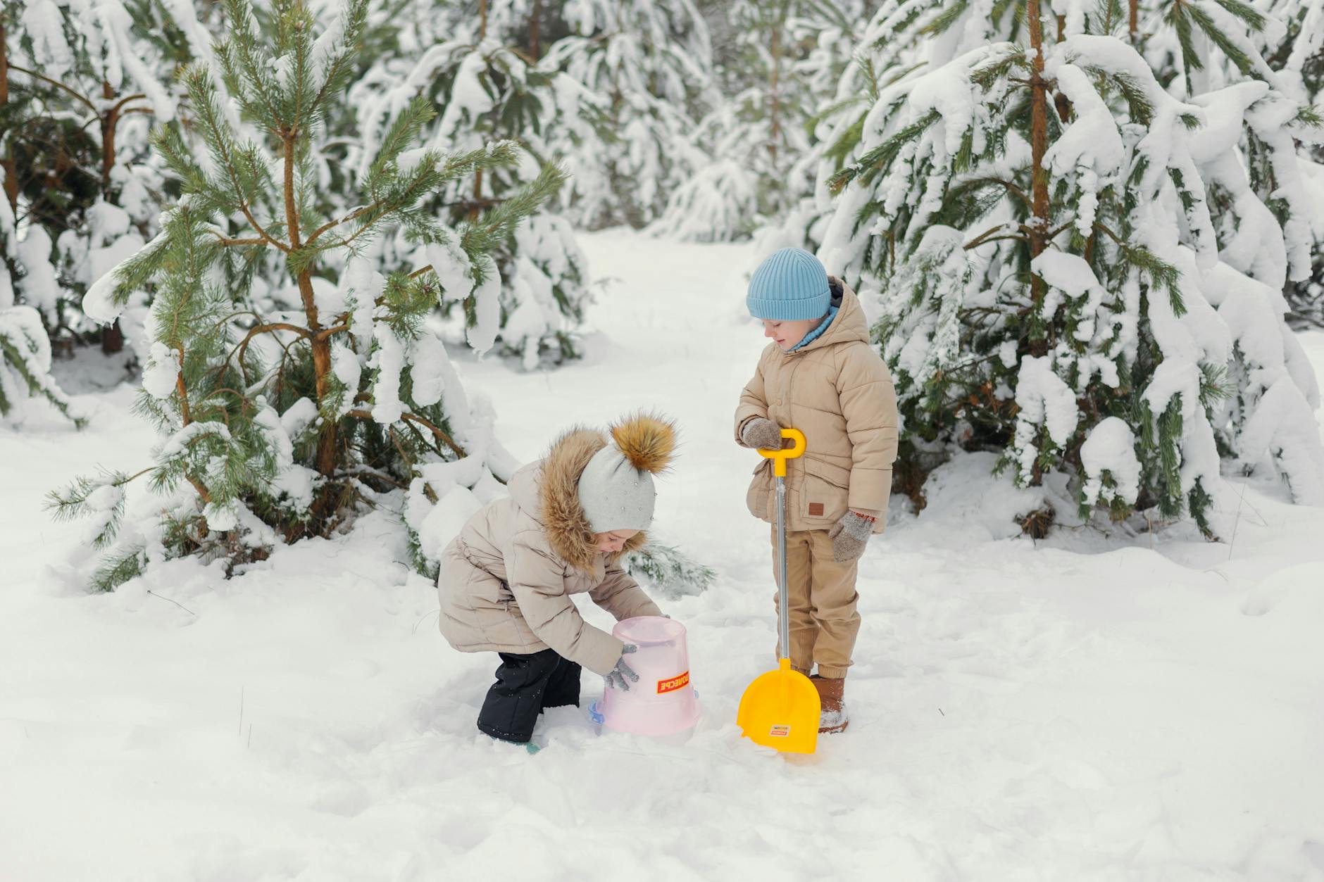 Two children having fun in a snowy forest, playing with a shovel and bucket. - creative indoor play snowy days