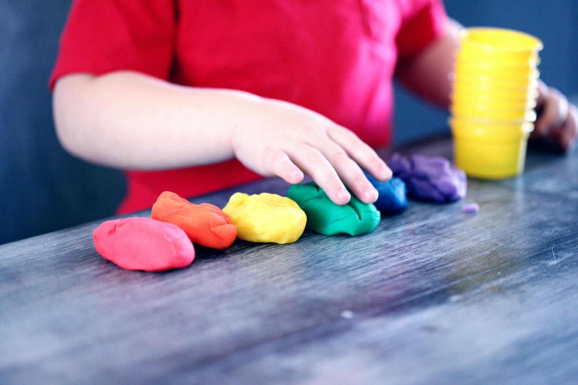 A young child with rainbow-colored modeling clay and stacking cups on a table indoors. - creative indoor play snowy days