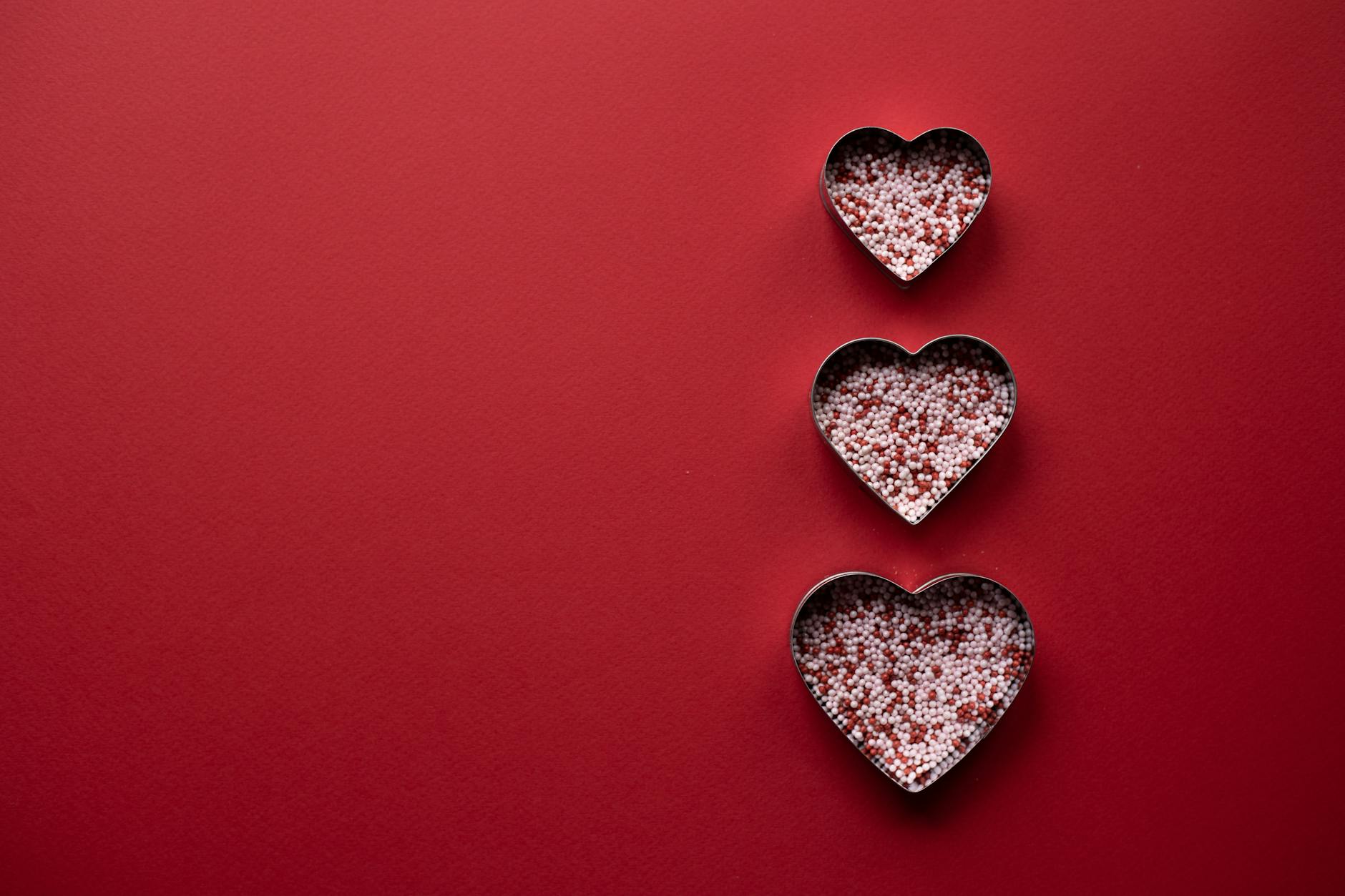 Top view of different hearts forms for cooking with sprinkling on red background - creative valentine's day ideas