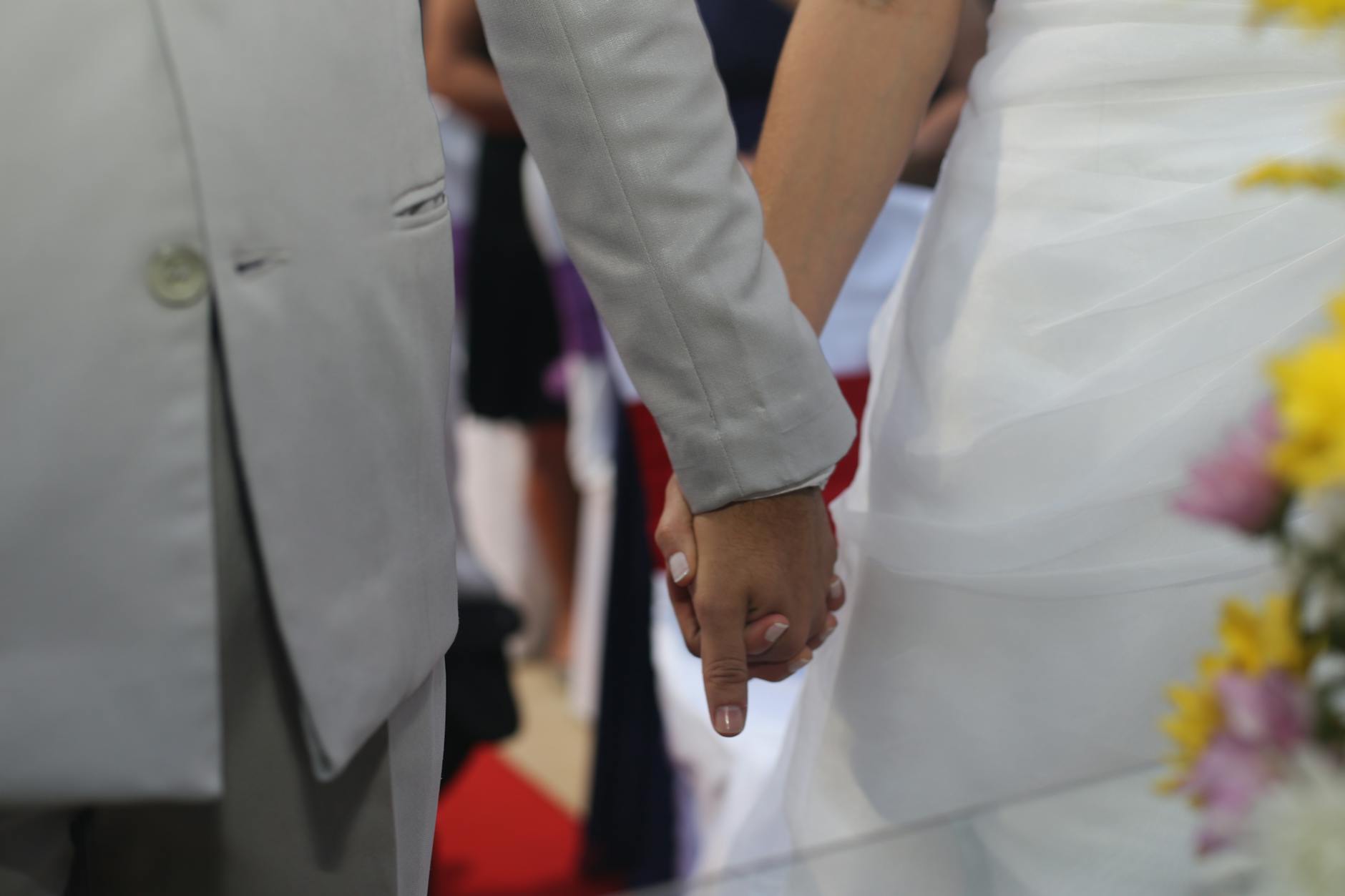 Close-up of a bride and groom holding hands during their wedding ceremony in a beautiful setting. - fear of commitment new relationship