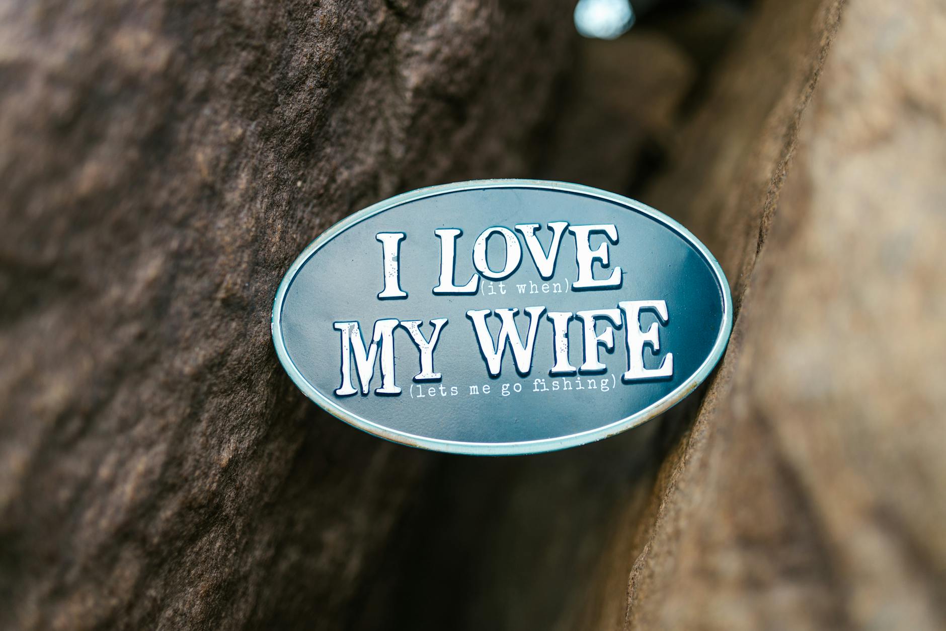 Metal pin on rock with playful text 'I Love My Wife (lets me go fishing)' - funny marriage advice