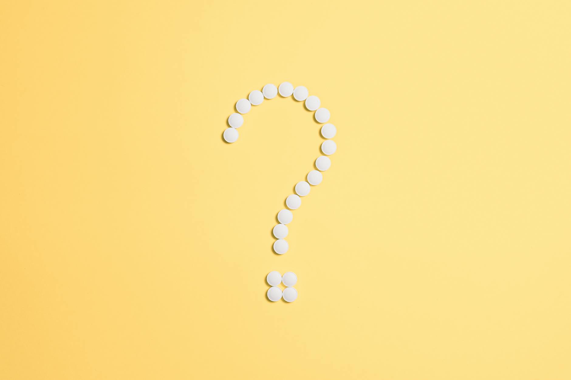 White pills arranged into a question mark shape on a vibrant yellow background. - good first date questions