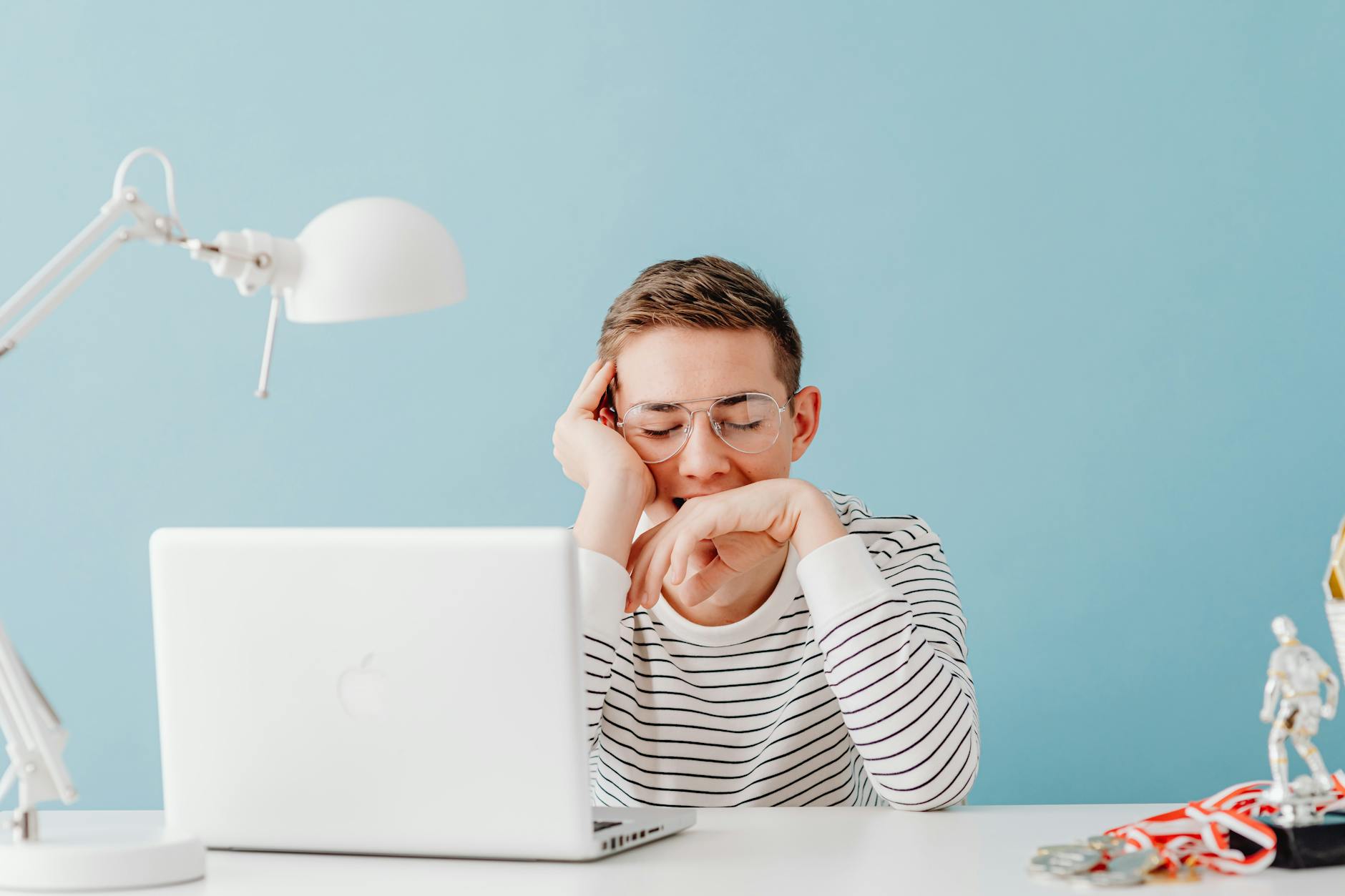 Young man in glasses yawning at desk with laptop and lamp, looking tired. - kids winter break boredom