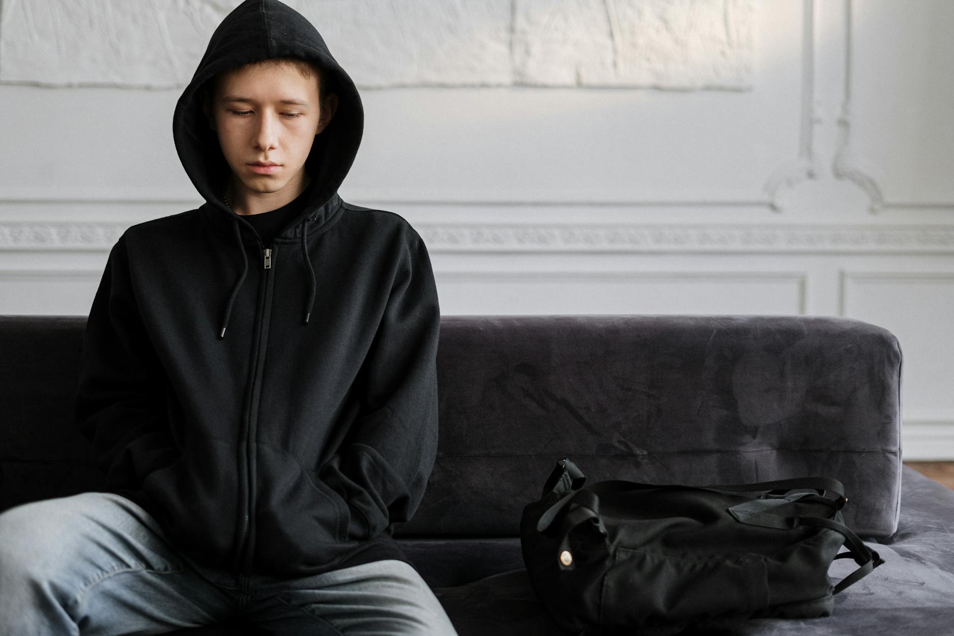 Young teen wearing hoodie sitting pensively on couch indoors. - light therapy for sad