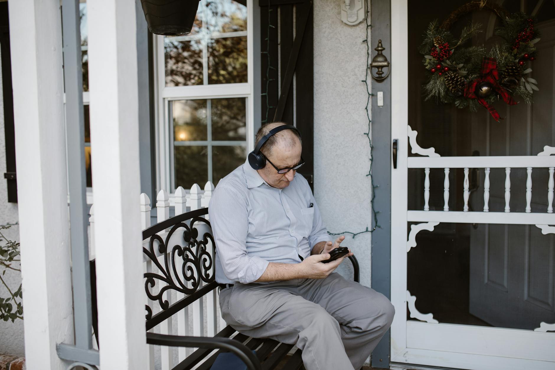 Elderly man enjoying music on porch, wearing headphones and checking phone. - long distance winter travel