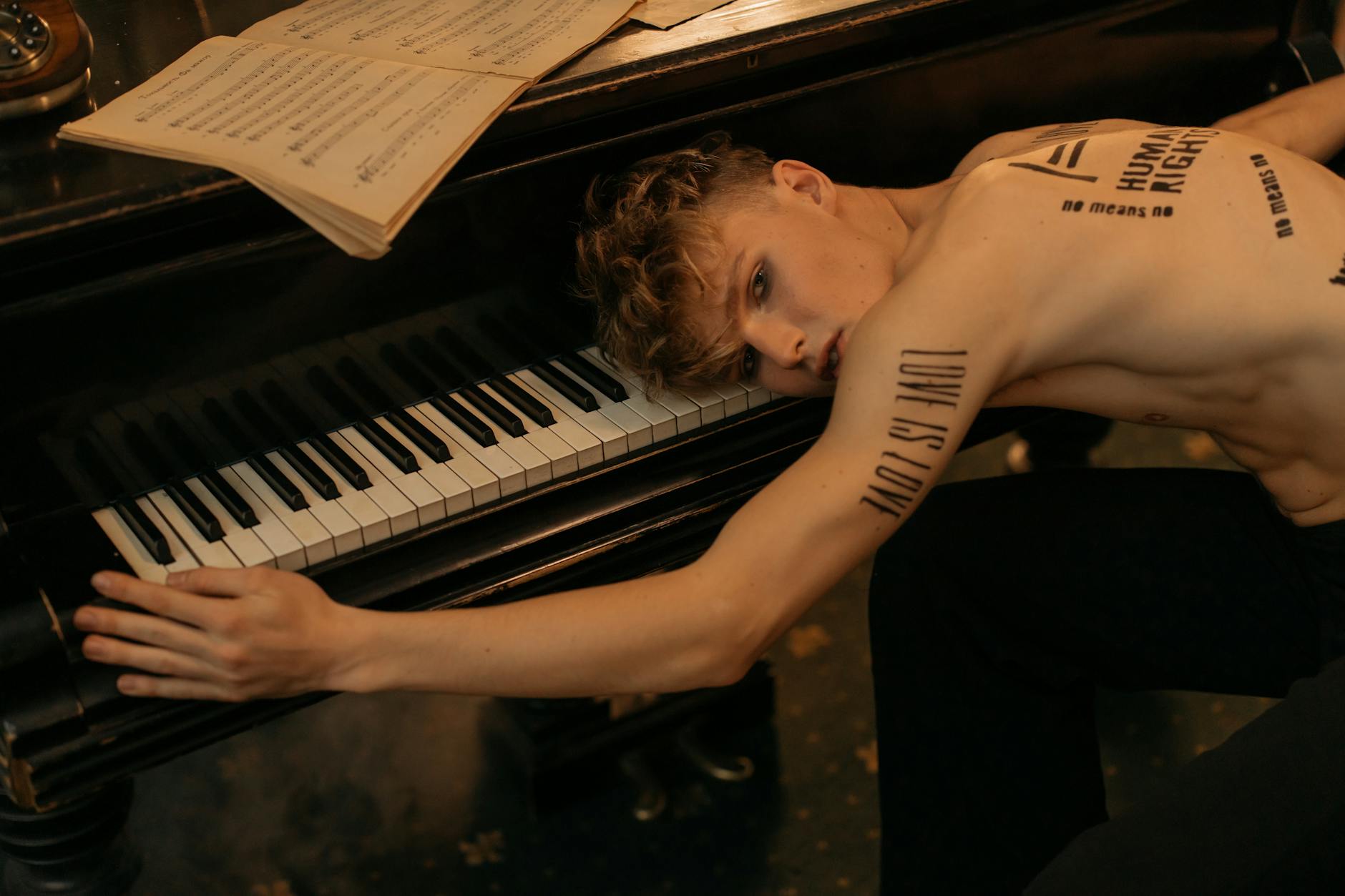 A shirtless tattooed man lies on a piano, merging music and art. - love bombing meaning