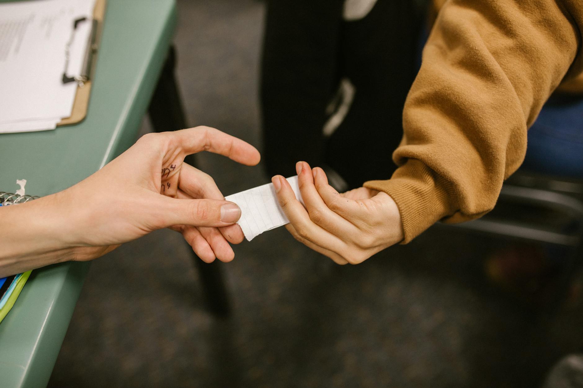 Close-up of two hands exchanging a small paper in a classroom setting, symbolizing discreet communication. - love language quiz
