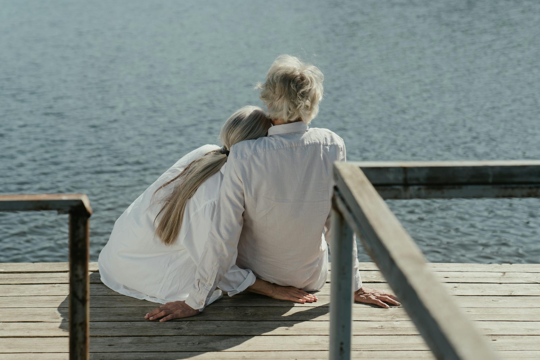 A senior couple enjoys a peaceful moment sitting together on a wooden dock by the lake, symbolizing enduring love. - maintain romance long term