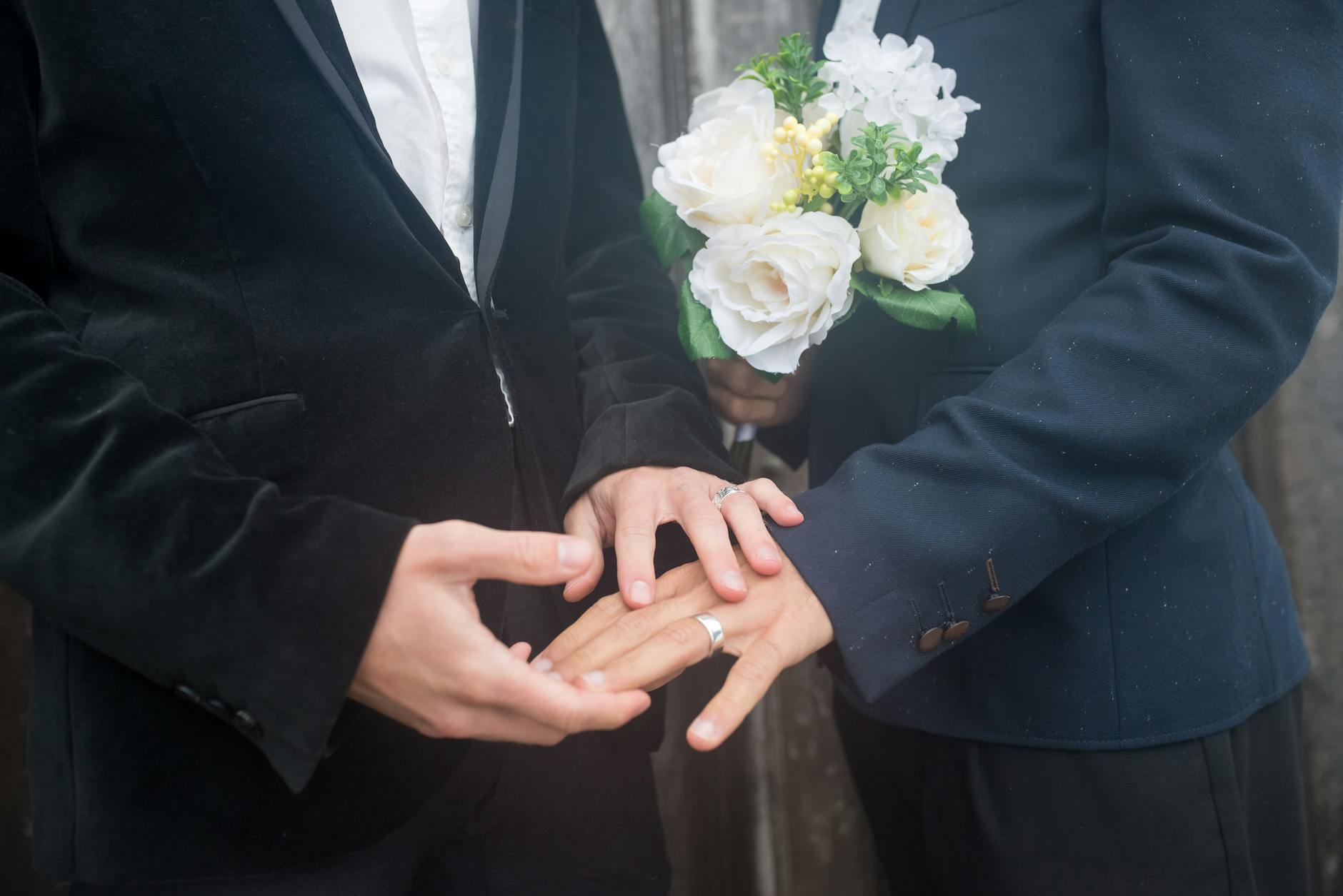 Close-up of two grooms holding hands with wedding rings and bouquet, symbolizing love and commitment. - marriage advice for newlyweds