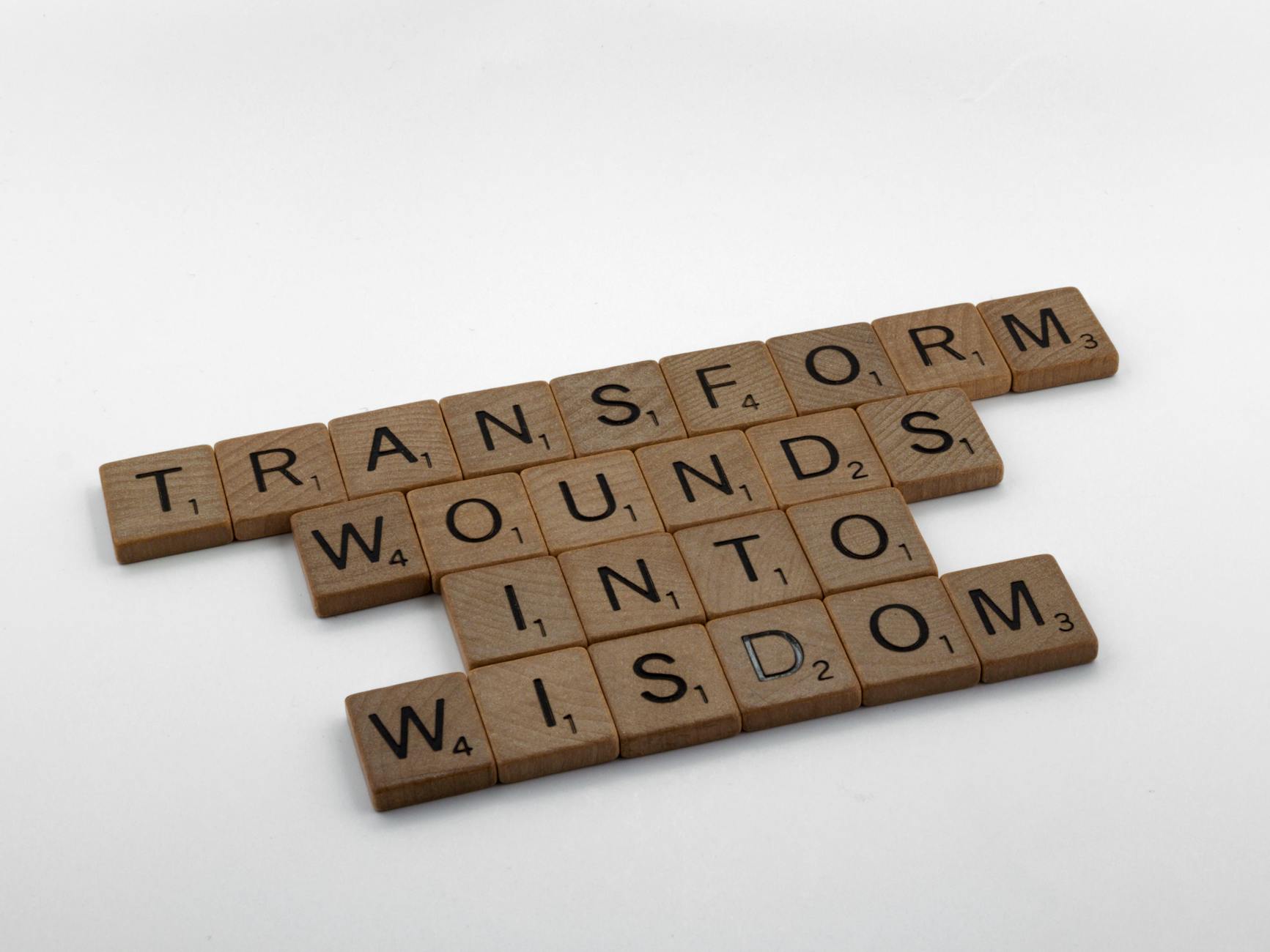 Wooden Scrabble tiles spelling 'Transform Wounds into Wisdom' on a neutral background. - marriage advice quotes