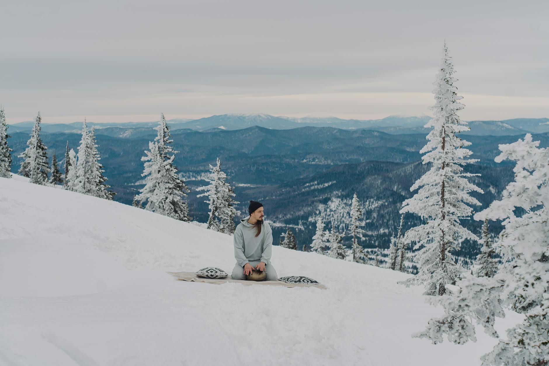 A man meditates peacefully on a snowy mountainside surrounded by frosted pines. - mindfulness for winter blues