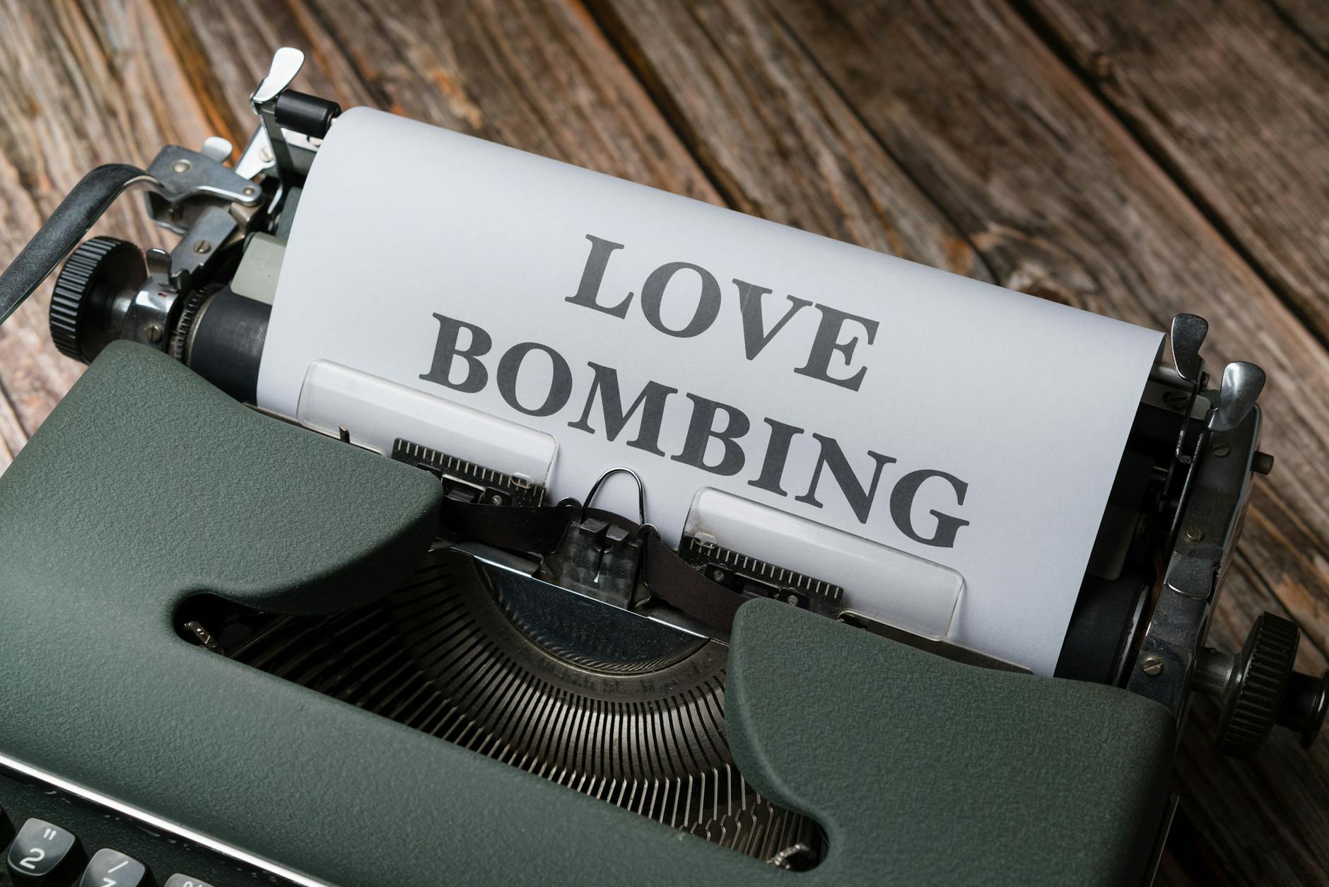 Close-up of a vintage typewriter printing 'Love Bombing' on paper, placed on a wooden desk. - narcissistic abuse recovery