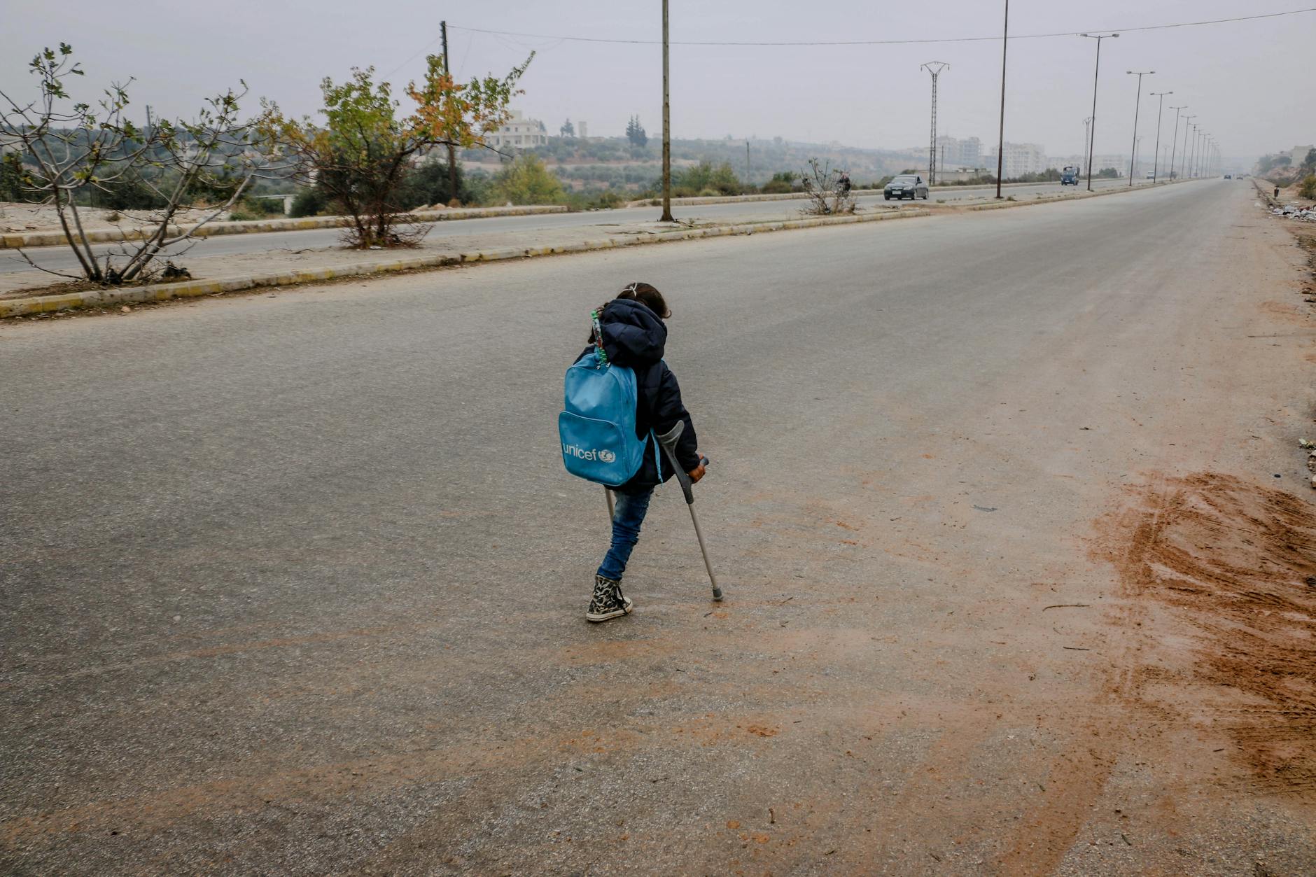 A young child with a crutch walking on a rural road in Idlib, Syria, symbolizing resilience. - overcome winter isolation