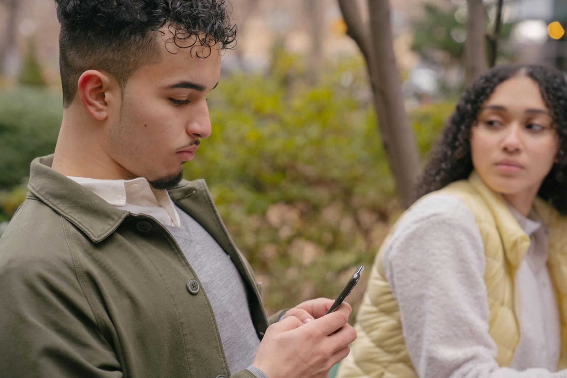 A young couple sitting outdoors with a smartphone, capturing casual moments and emotions. - overcoming jealousy in relationships