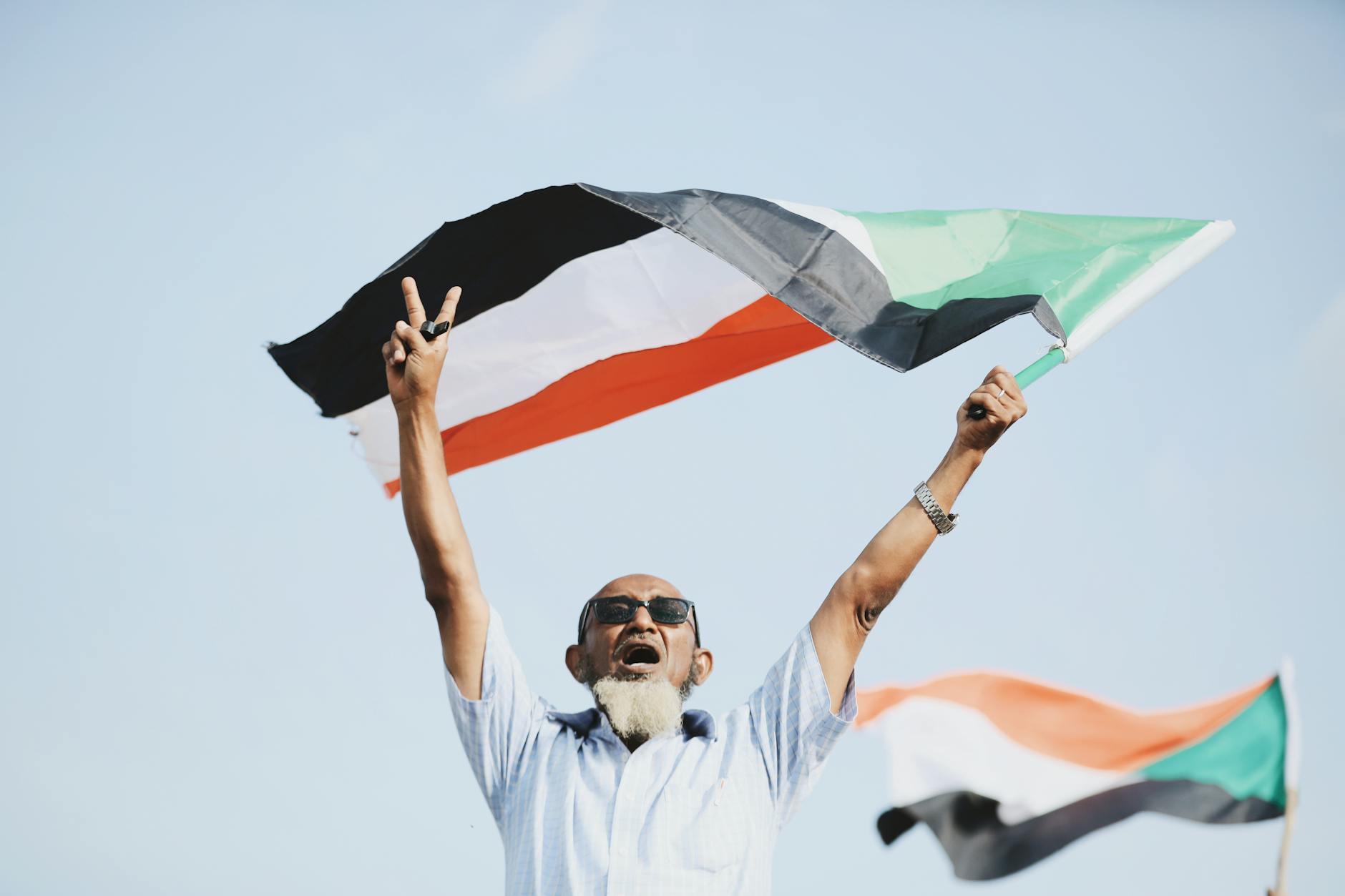 A joyful man holds the Sudanese flag, celebrating outdoors with a victory sign. - overcoming winter blues