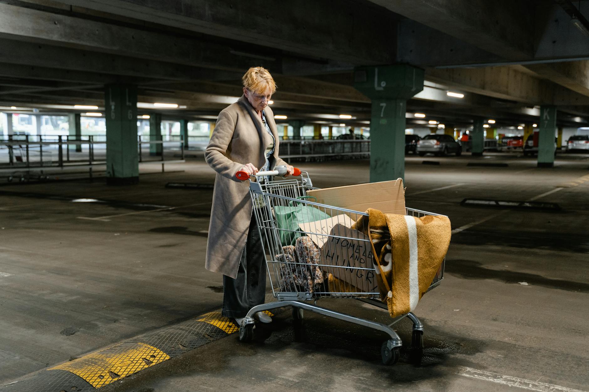 Elderly woman pushing shopping cart in empty parking garage, highlighting urban poverty. - overcoming winter loneliness