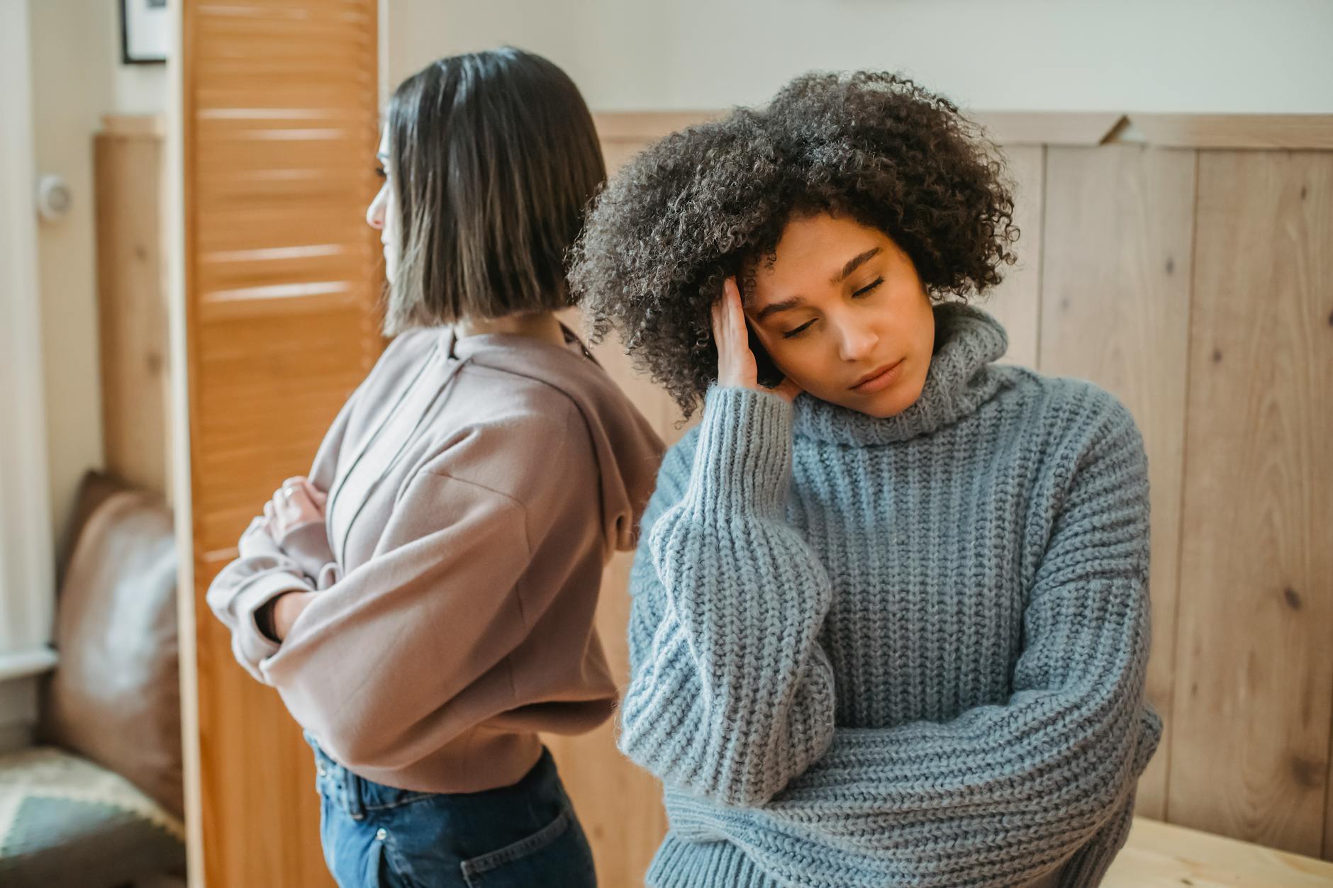 Upset African American woman with curly hair and offended female standing in light room with wooden wall while having conflict - post-holiday relationship regret