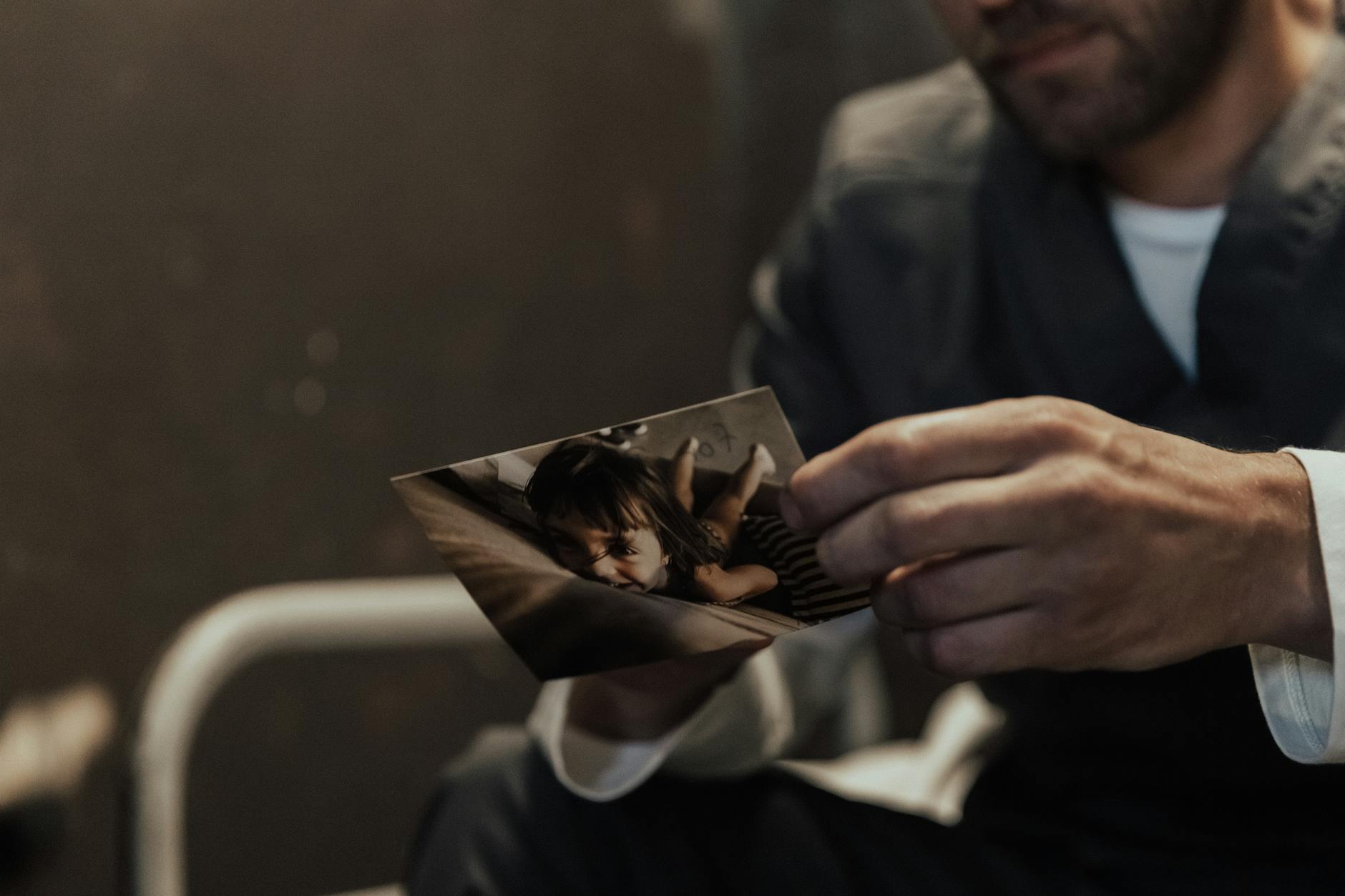 A man in prison uniform holds a photo of a child, evoking emotion and introspection. - post-holiday relationship regret