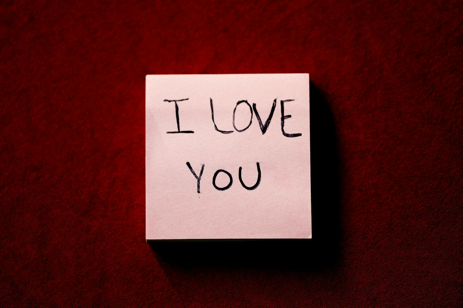 A close-up of a note with 'I Love You' written on it, placed on a red textured background. - post valentine's relationship expectations