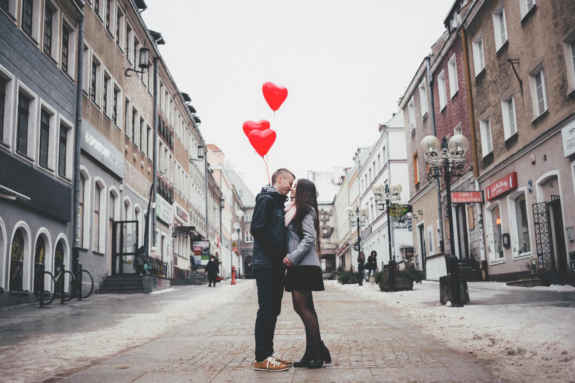 A loving couple shares a kiss with heart-shaped balloons in a charming urban street setting. - post valentine's relationship expectations