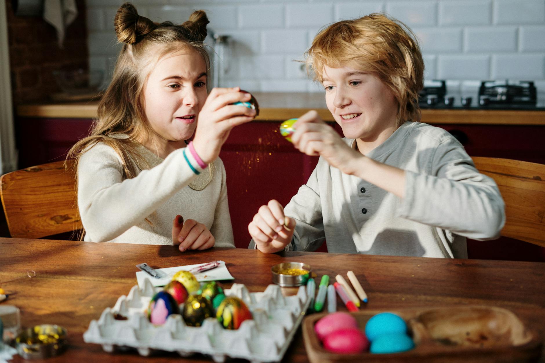 Two children sitting at a wooden table enjoying Easter egg decorating indoors. - preparing kids for spring transition