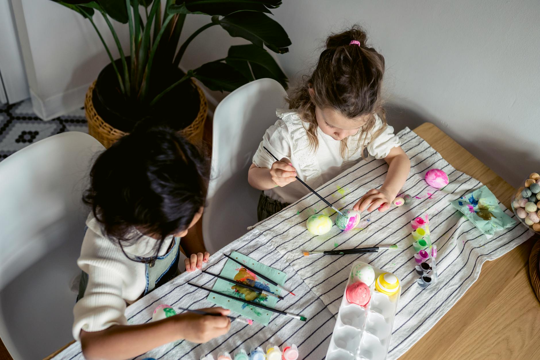 Two children engaged in painting Easter eggs indoors with colorful paints and brushes, evoking creativity and fun. - preparing kids for spring transition