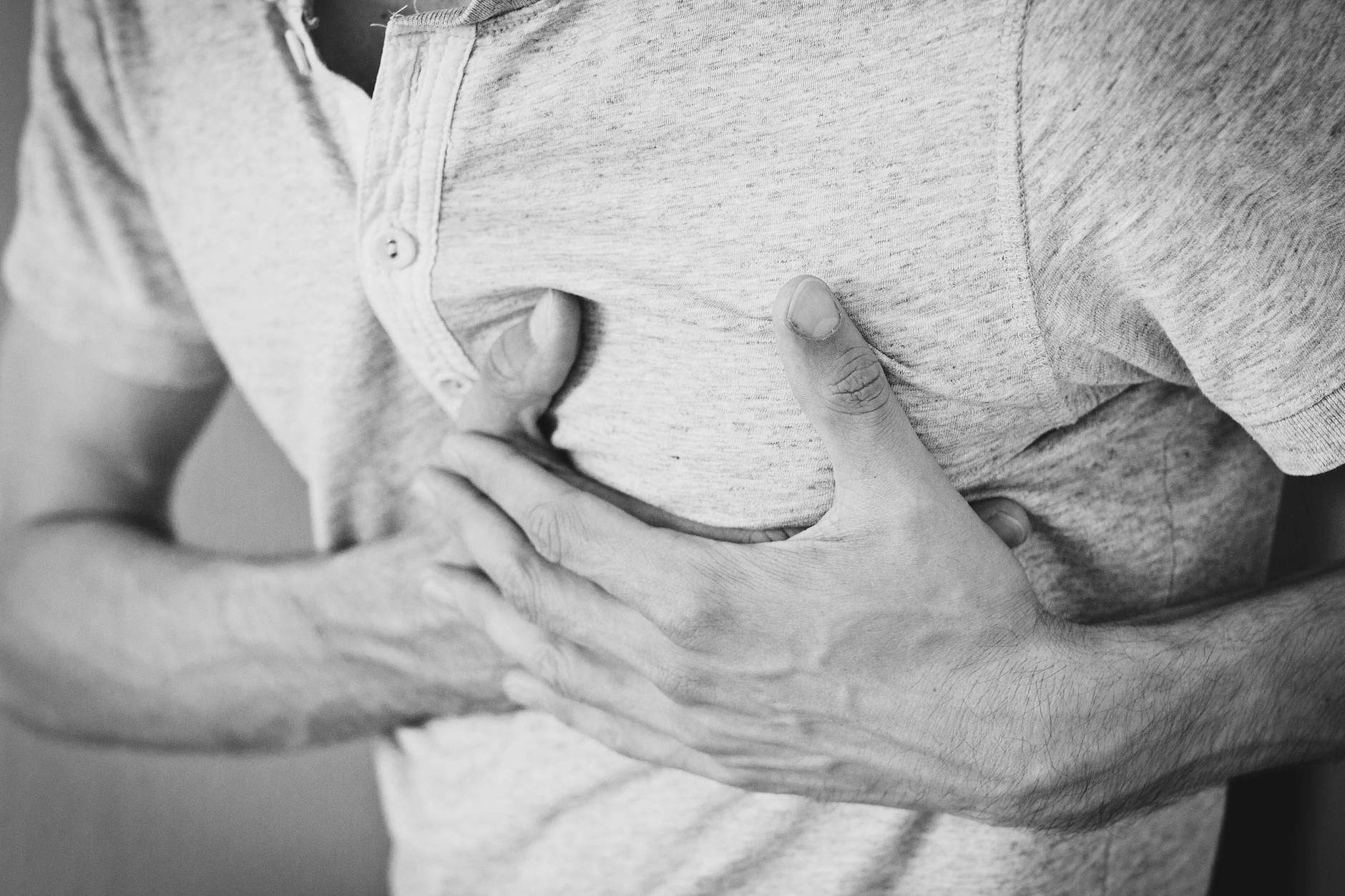 Black and white photo of a man clutching his chest, indicating discomfort or pain. - relationship anxiety symptoms