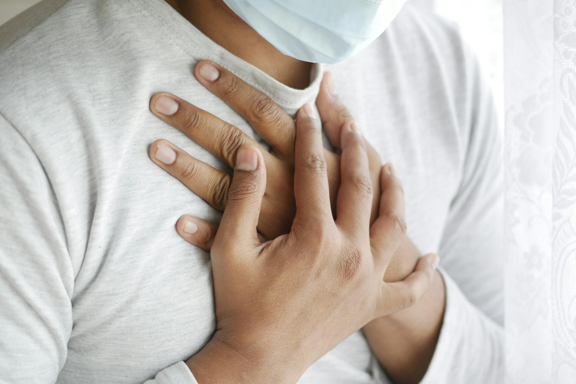 Close-up image of a masked person holding chest, symbolizing health concerns. - relationship anxiety symptoms