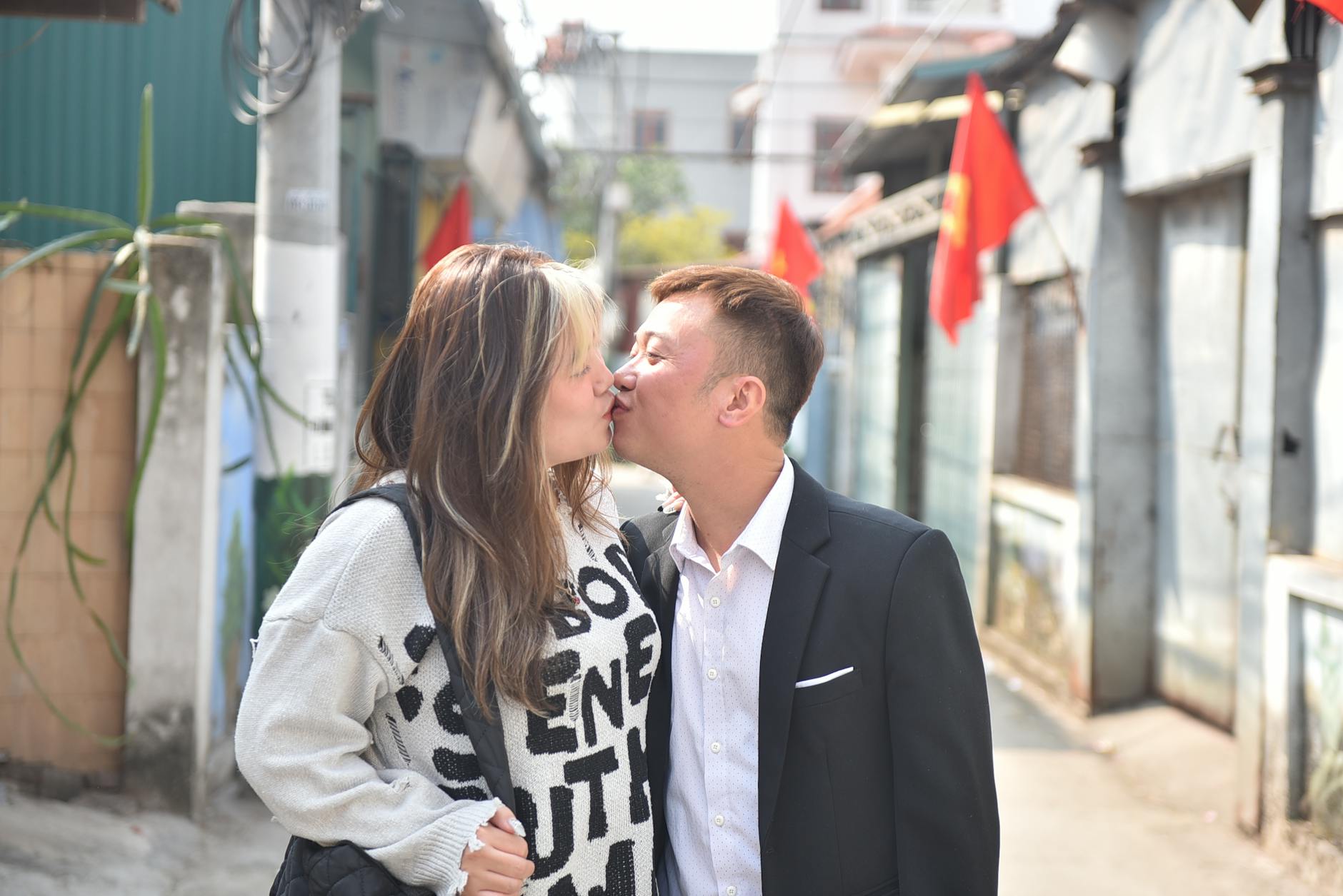 A couple shares a tender kiss on a sunny urban street lined with red flags. - relationship red flags